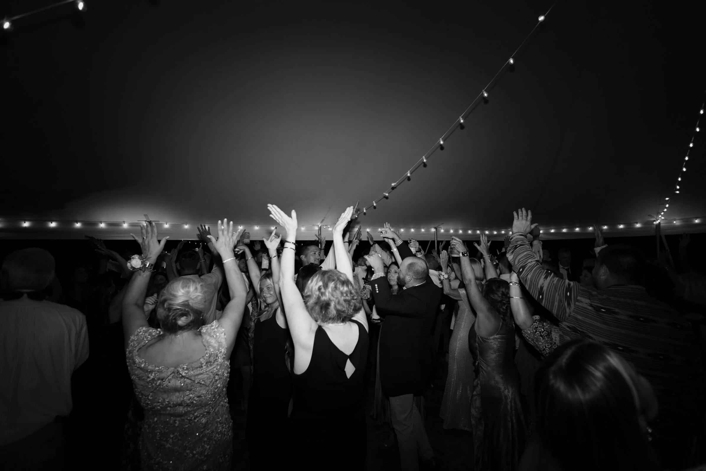 People dancing and raising their hands under a string of lights at a celebration or party.