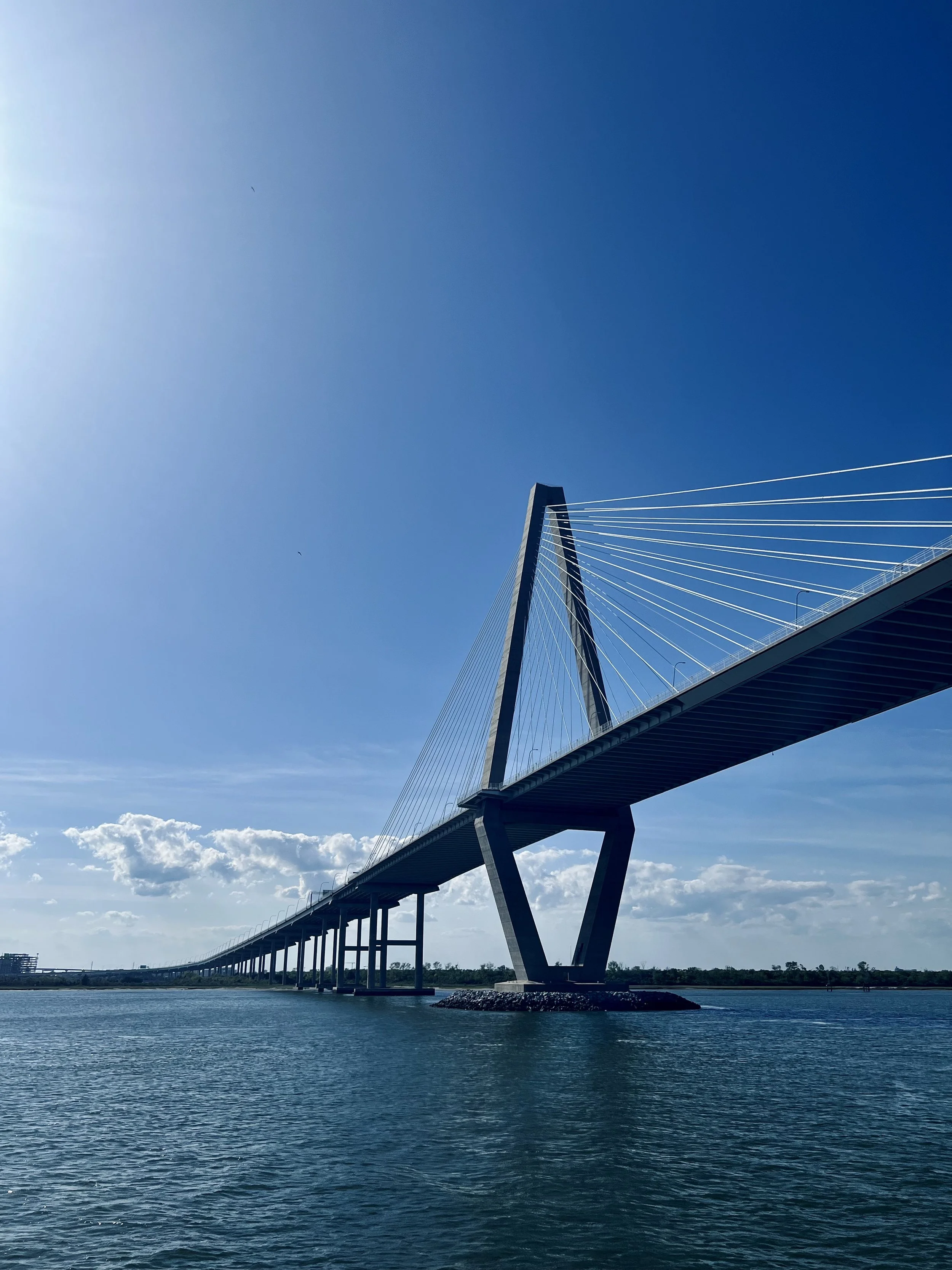 A modern cable-stayed bridge with a tall central tower, spanning over a body of water on a clear, sunny day.