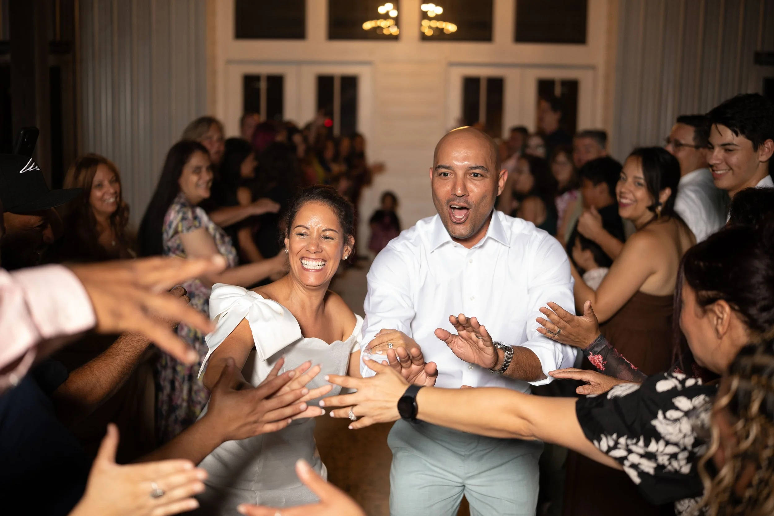 A group of people dancing and having fun at a celebration or party indoors, with a woman and man in the center smiling and clapping.