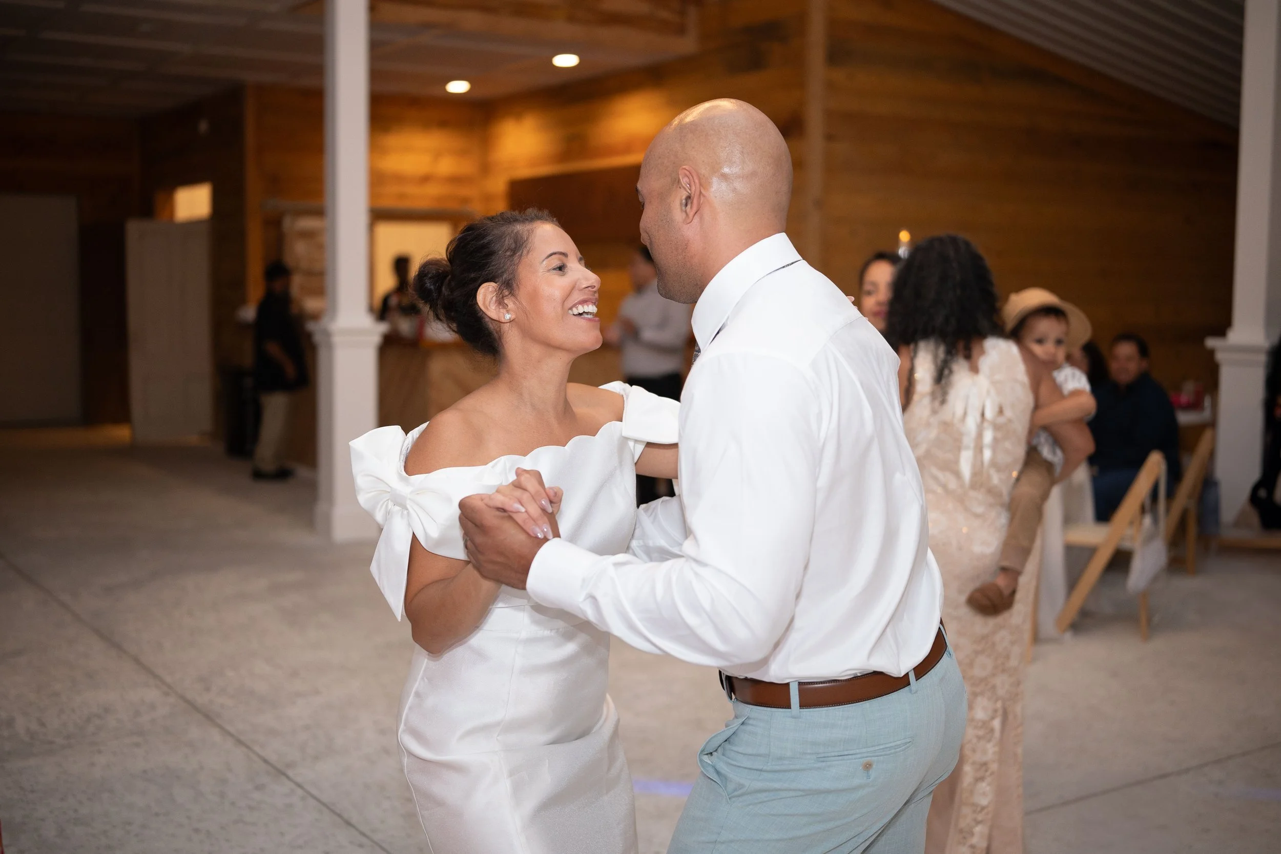 A woman and a man are dancing together at a wedding reception, smiling at each other and holding hands.