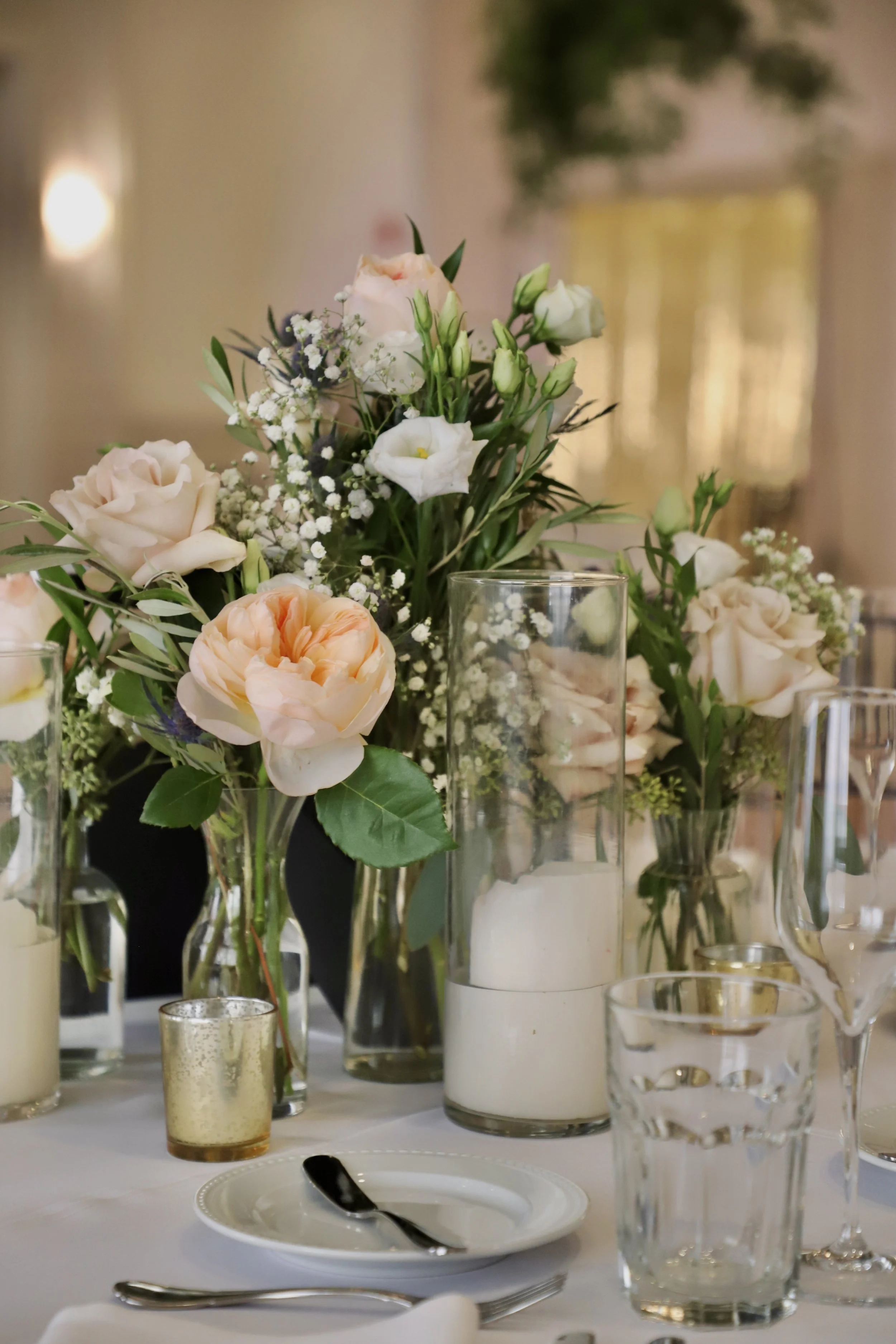 Elegant table setting with floral centerpieces featuring light pink and white flowers, candles, and glassware.