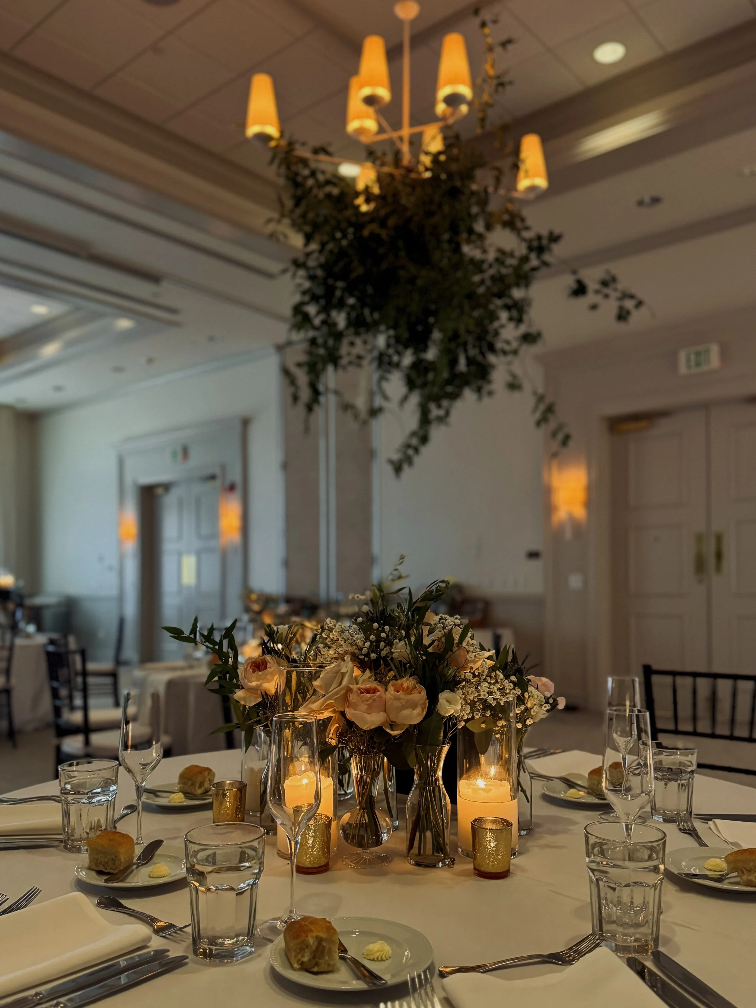 Elegant banquet table with floral centerpiece, candles, glasses, plates, and silverware in a decorated dining room.