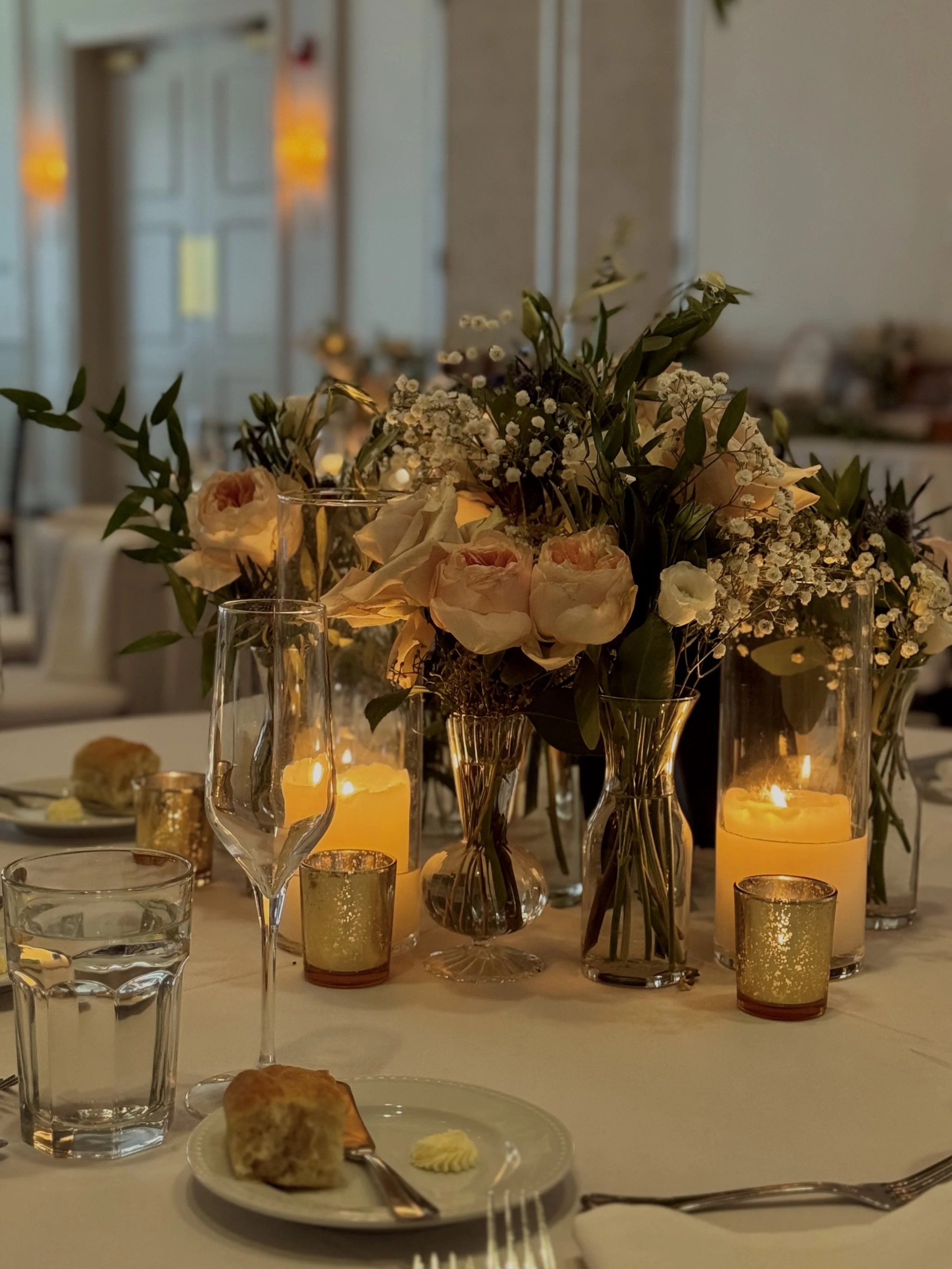 Table decorated with flowers and candles at an elegant event, with a plate of food and glassware.