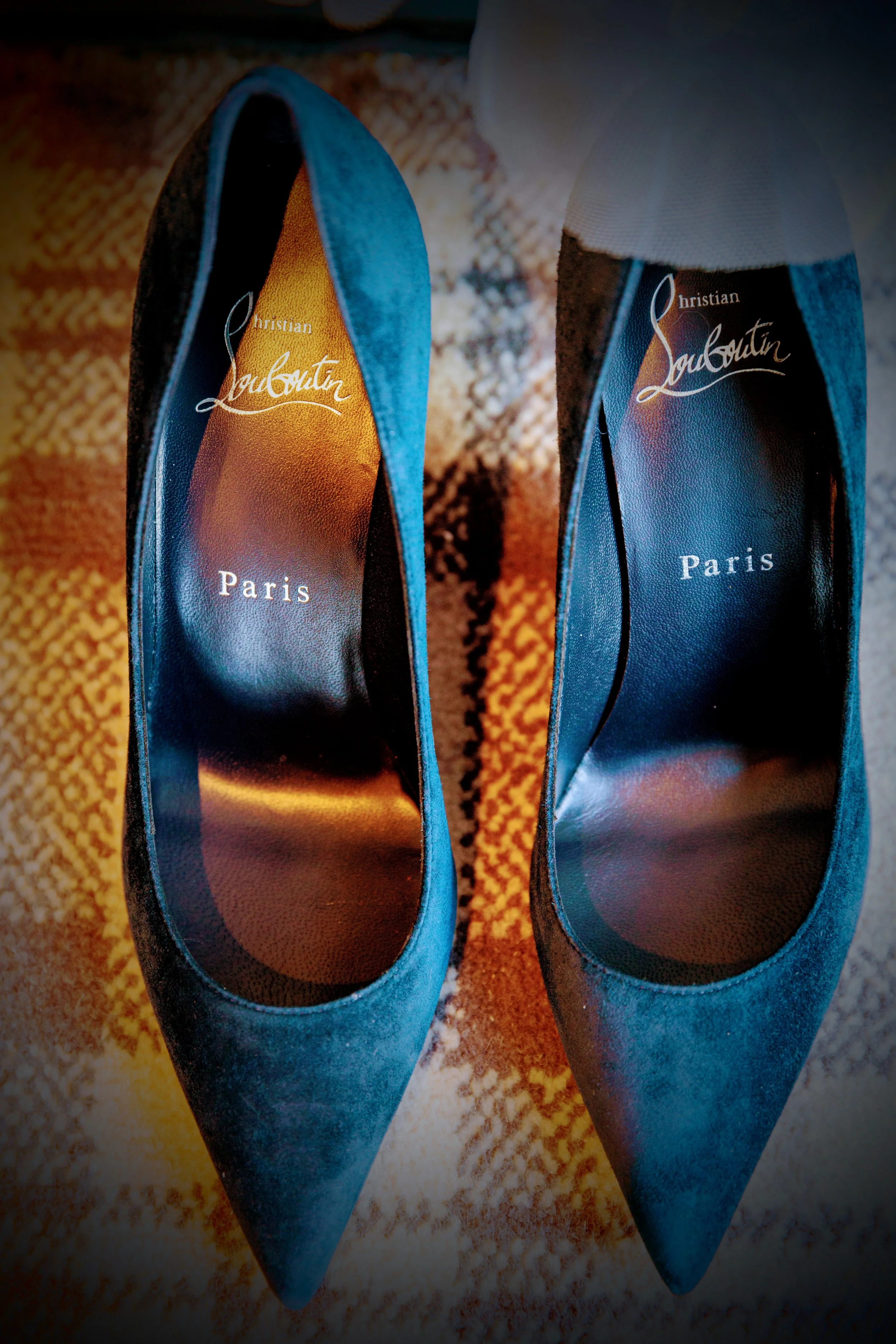 Pair of blue Christian Louboutin high heels on a patterned carpet.