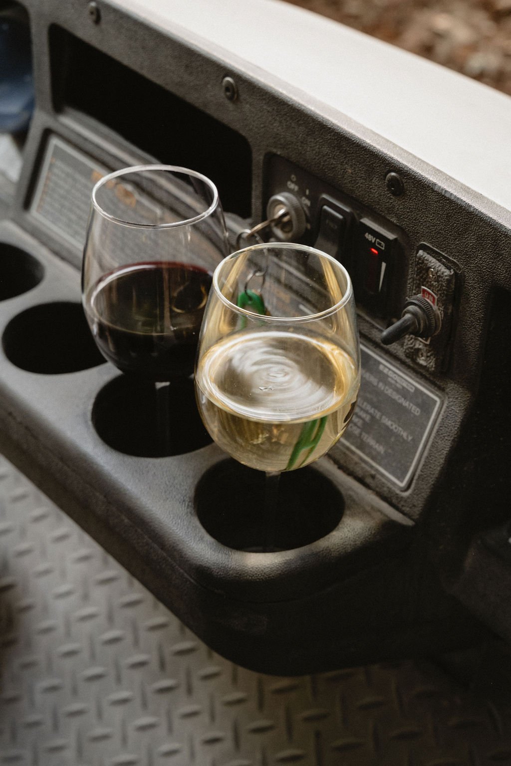 Two glasses, one filled with red wine and the other with white wine, are placed on a black surface with circular indents, in front of a vintage audio or speaker system.