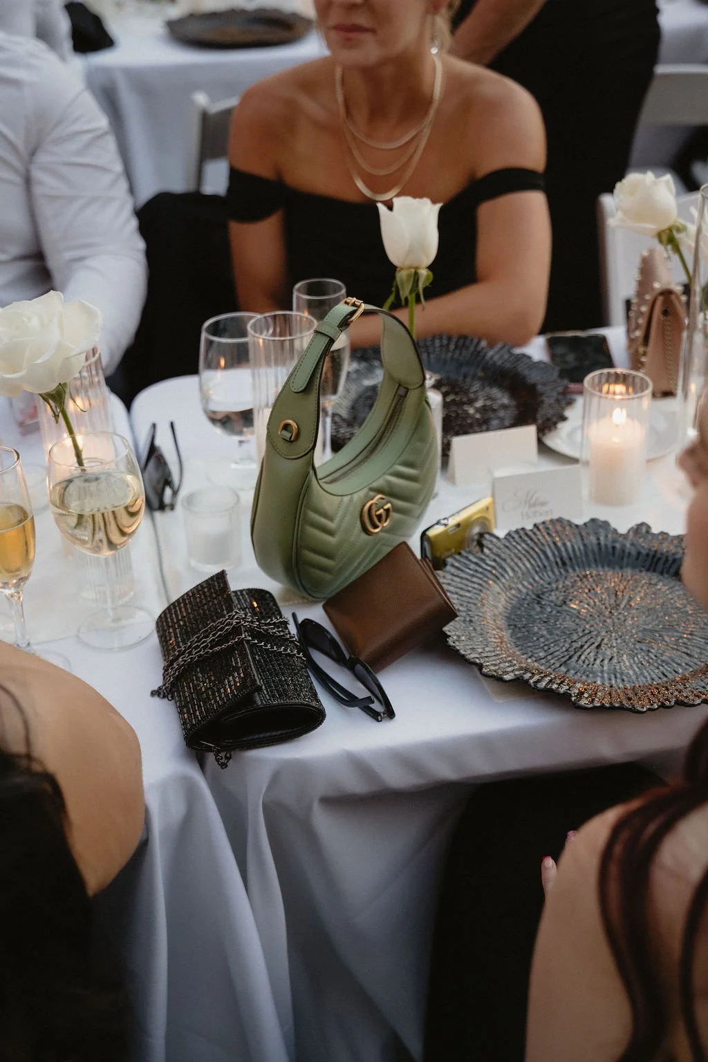 A formal dinner table setup with floral decorations, glasses, and handbags, during an event with women dressed in elegant attire.