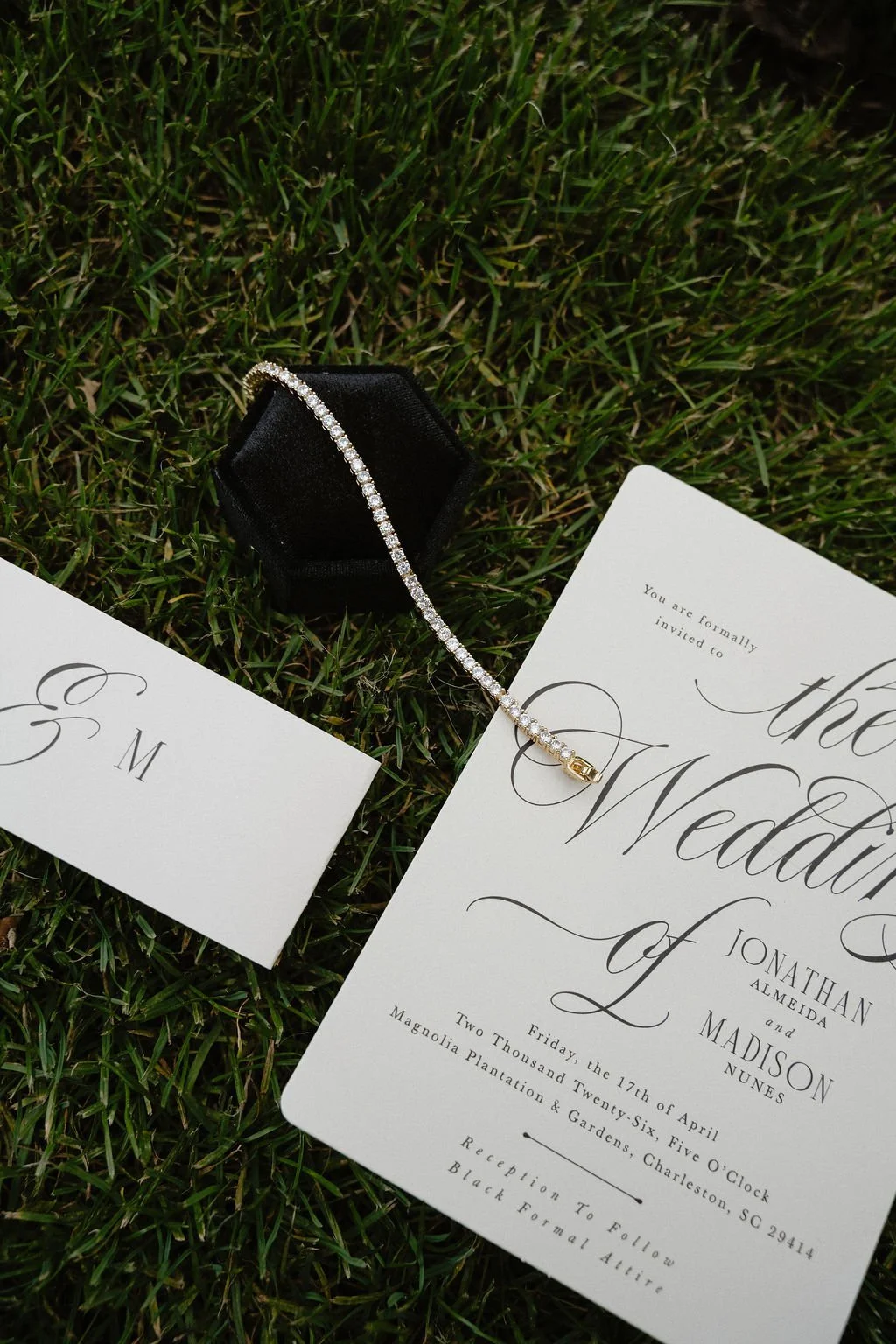 Wedding invitation with an engagement bracelet and a small card on grass.