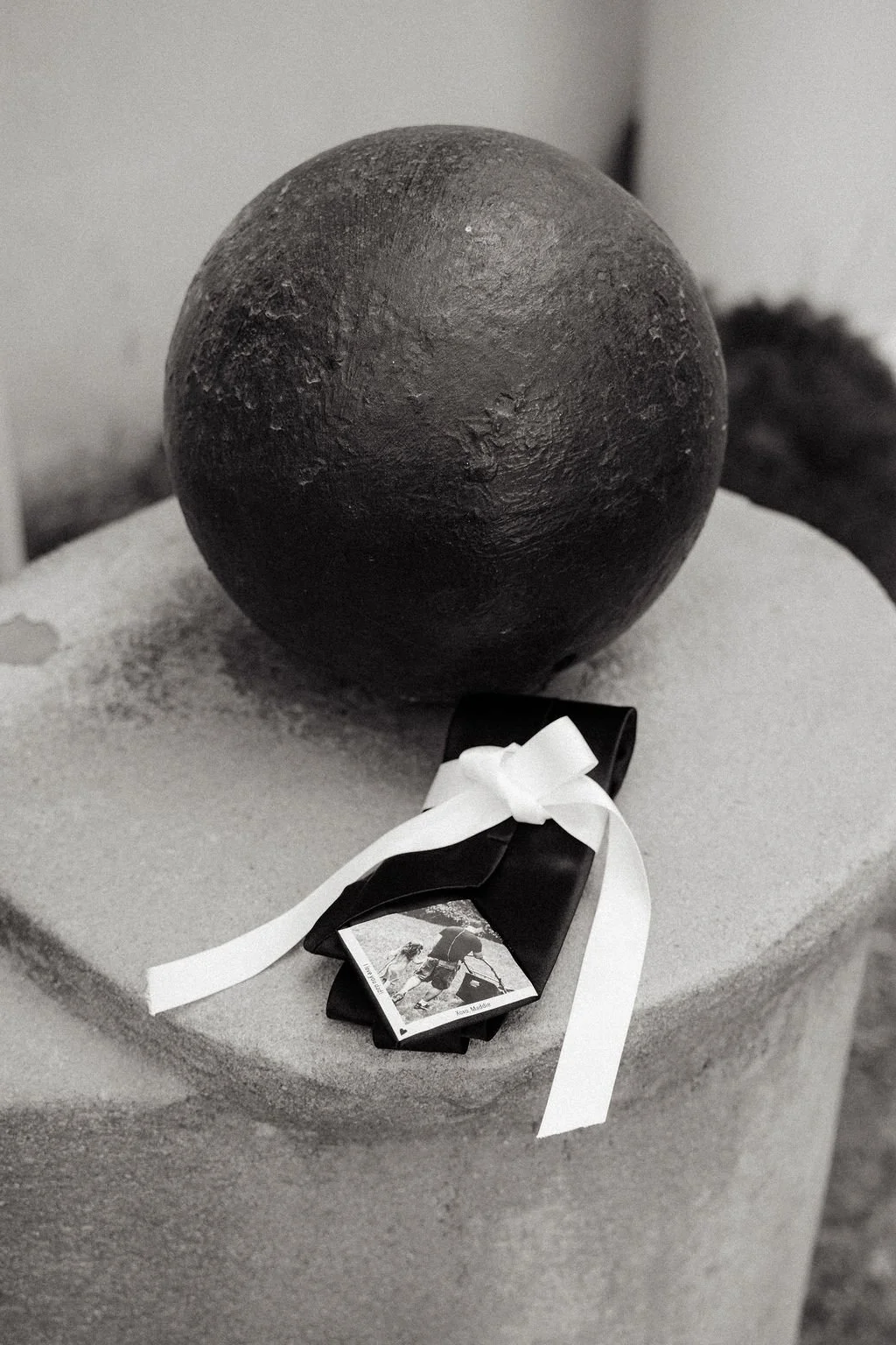 A black cannonball placed on a stone pedestal with a ribbon-tied card attached, alongside others in the background.