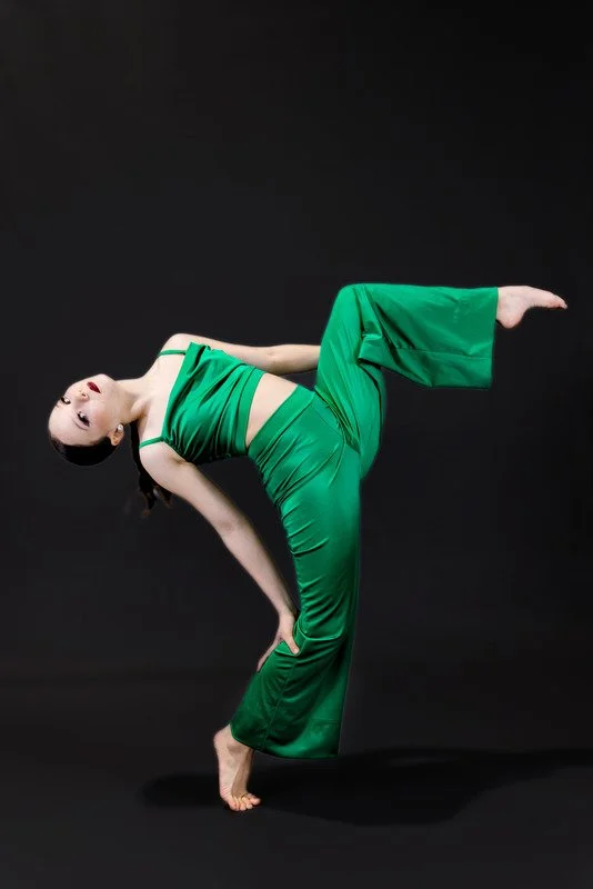 A woman performing a pose in a green outfit against a black background.