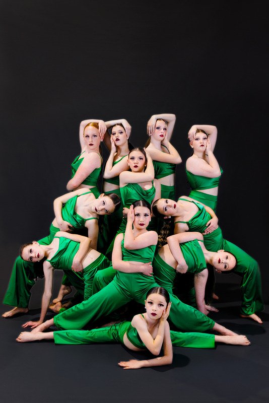 Group of young dancers in green costumes posing against a black background.