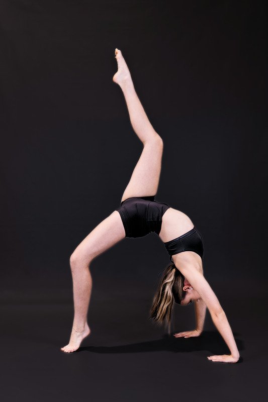 A woman performing a yoga pose called a forearm stand against a black background.