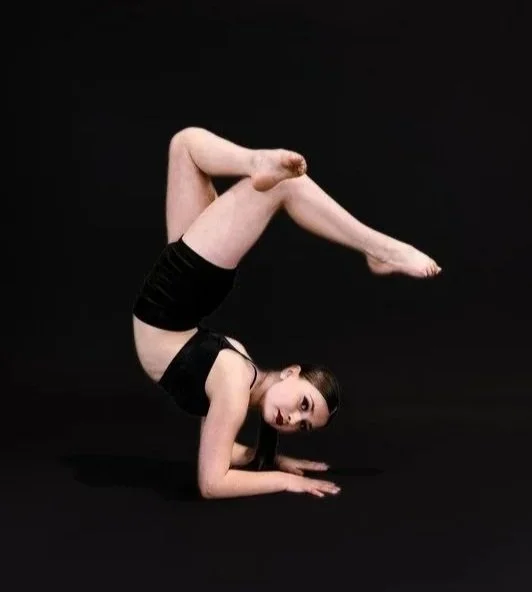 A woman performing a competitive gymnastics move on a black background.