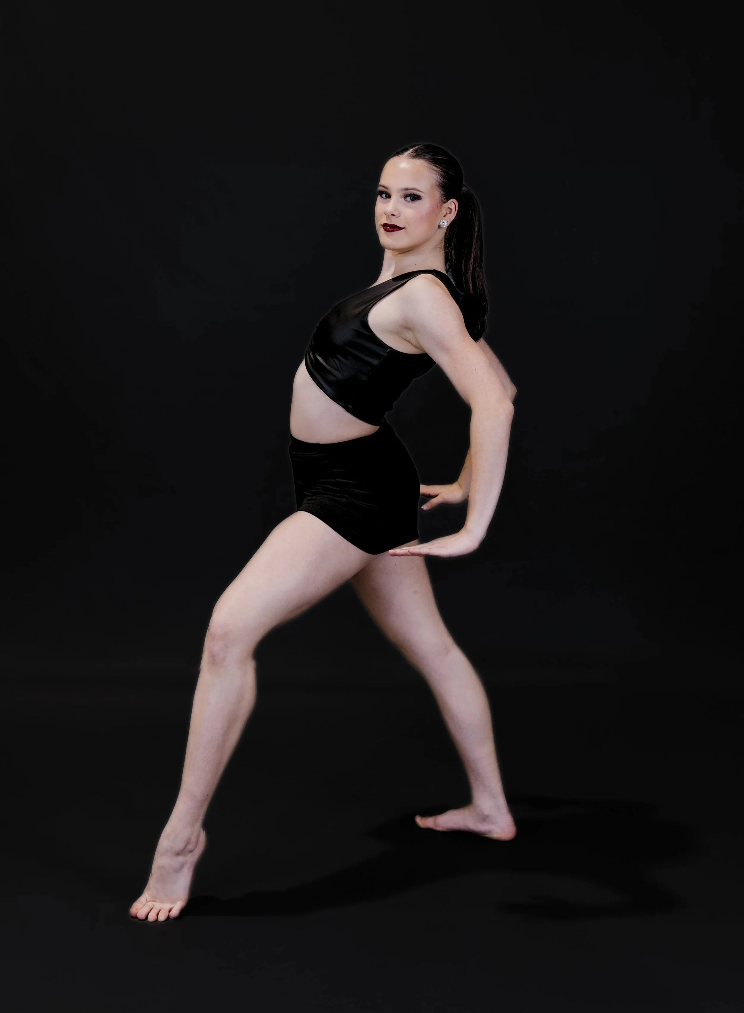 A female dancer in black dance attire posing against a black background.