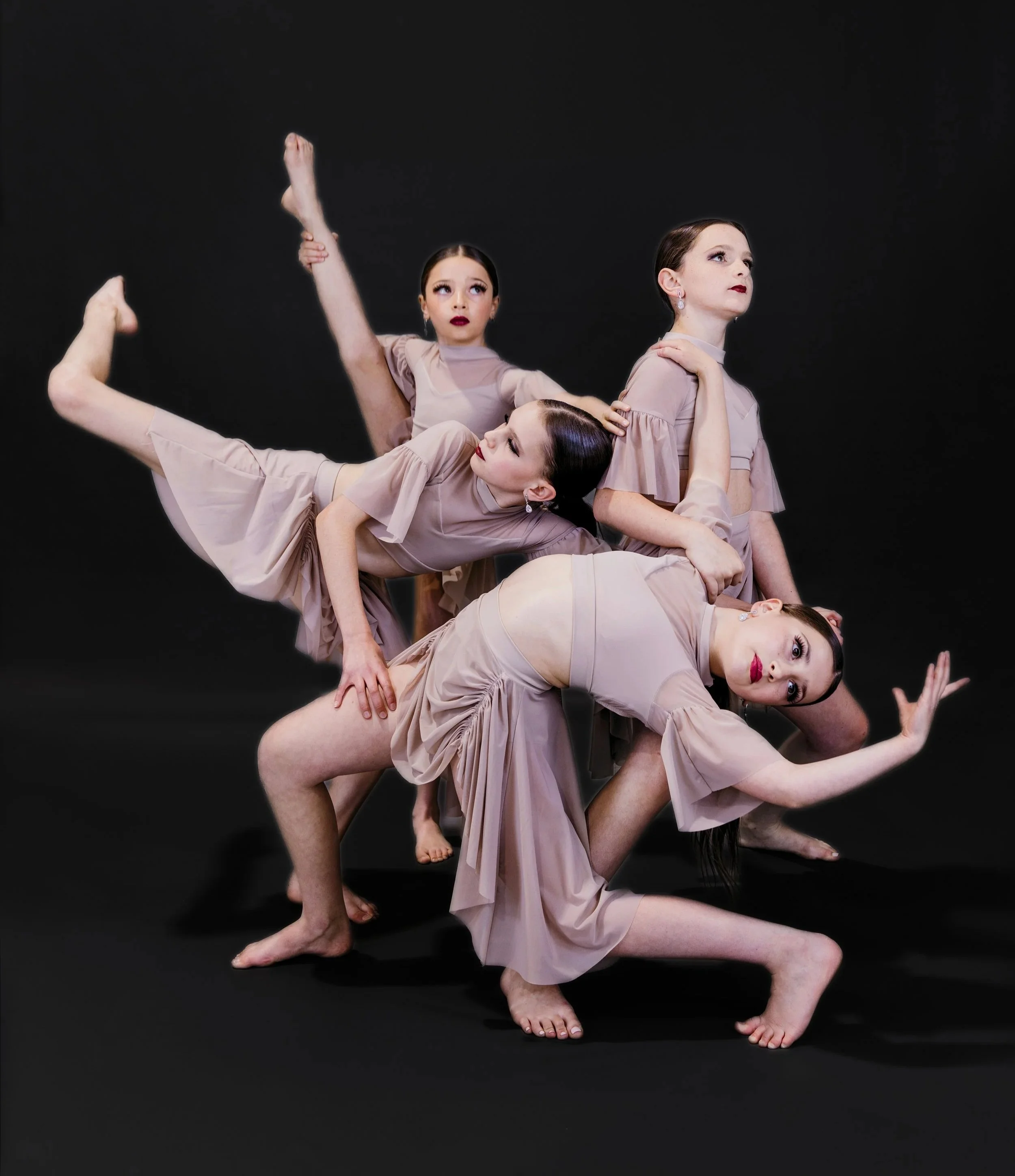 Four women practicing ballet in nude-colored costumes performing a complex dance pose against a black background.