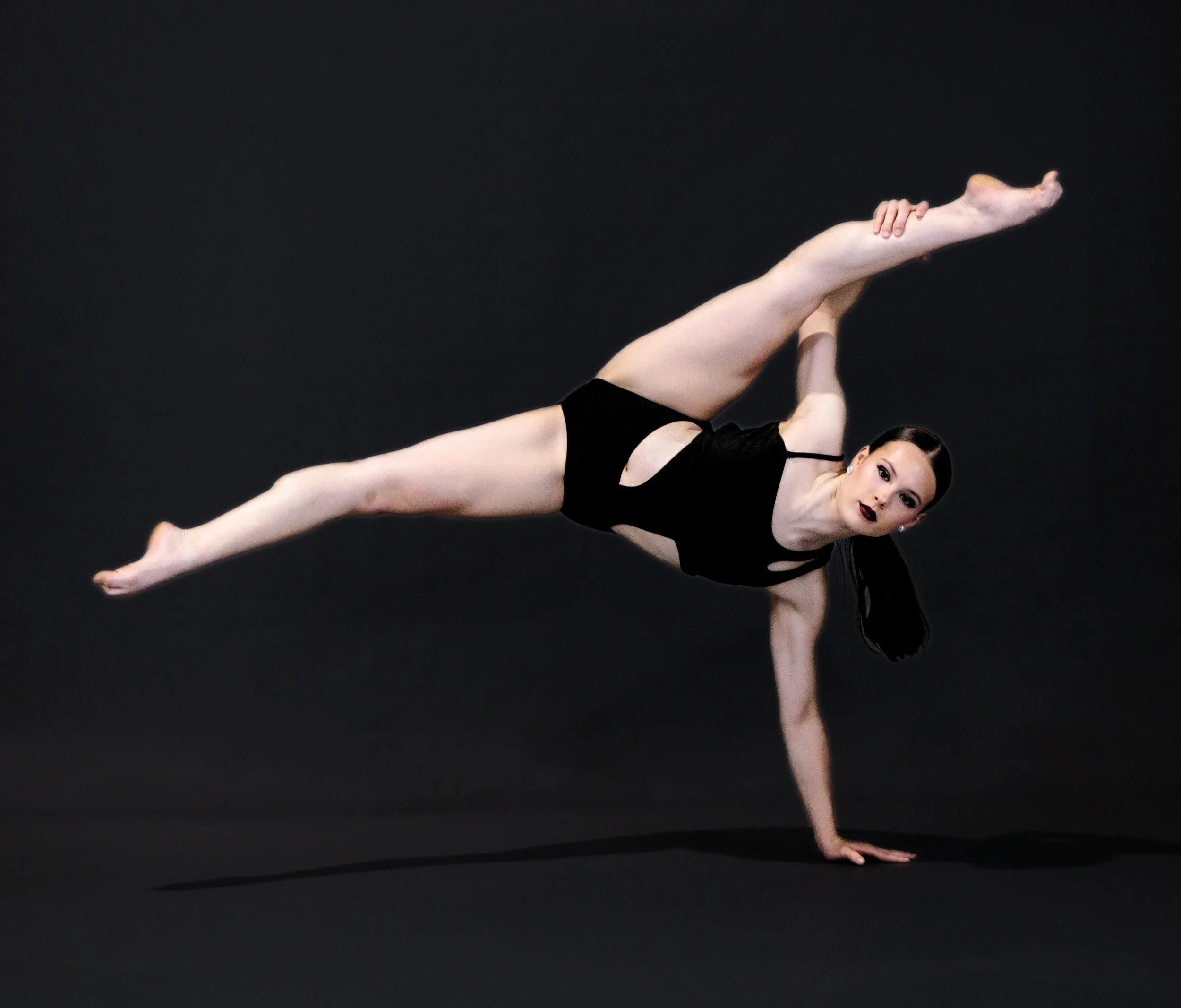 A female gymnast in a black leotard performing a handstand on a black background.