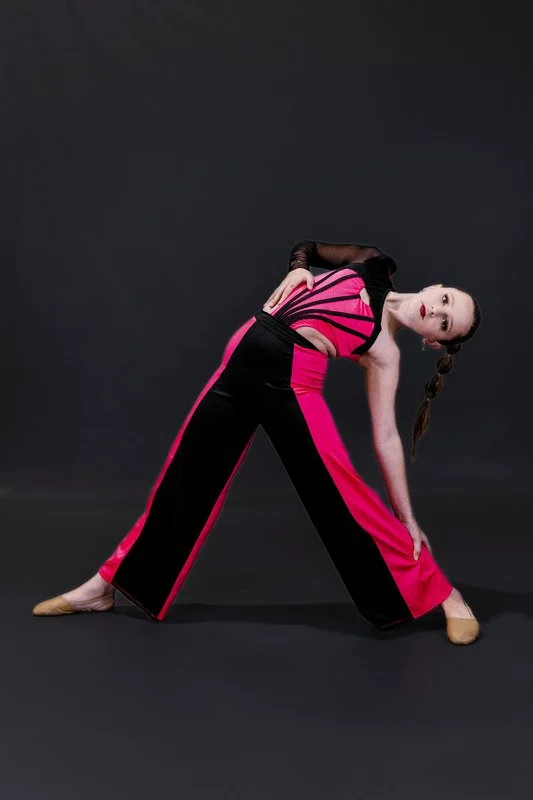 A woman in a colorful, fashionable outfit performing a dance pose against a black background.