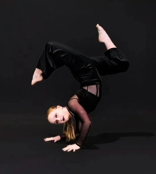 A young girl performing a handstand in a black outfit against a dark background.