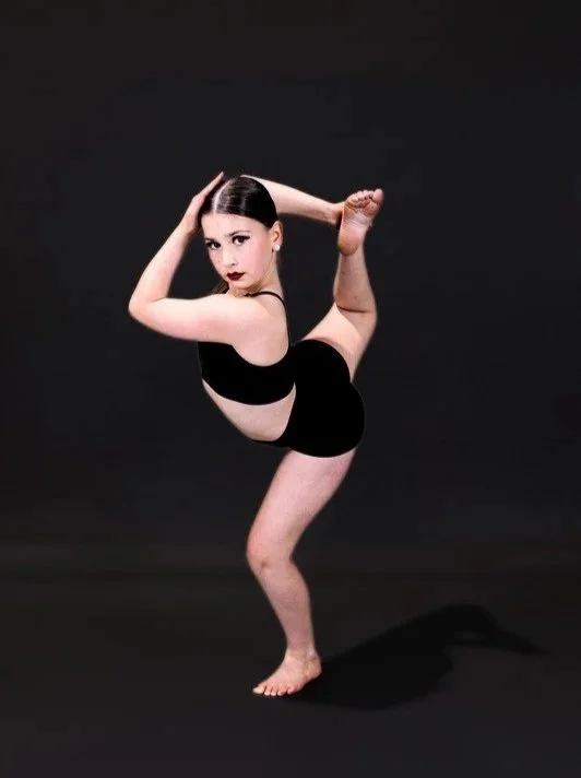 A woman with dark hair in a ponytail, wearing black athletic wear, performs a yoga pose on a black background.