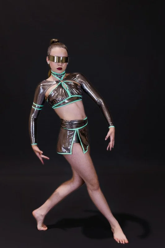 A person wearing futuristic metal-inspired clothing with reflective sunglasses, striking a dramatic pose against a black background.