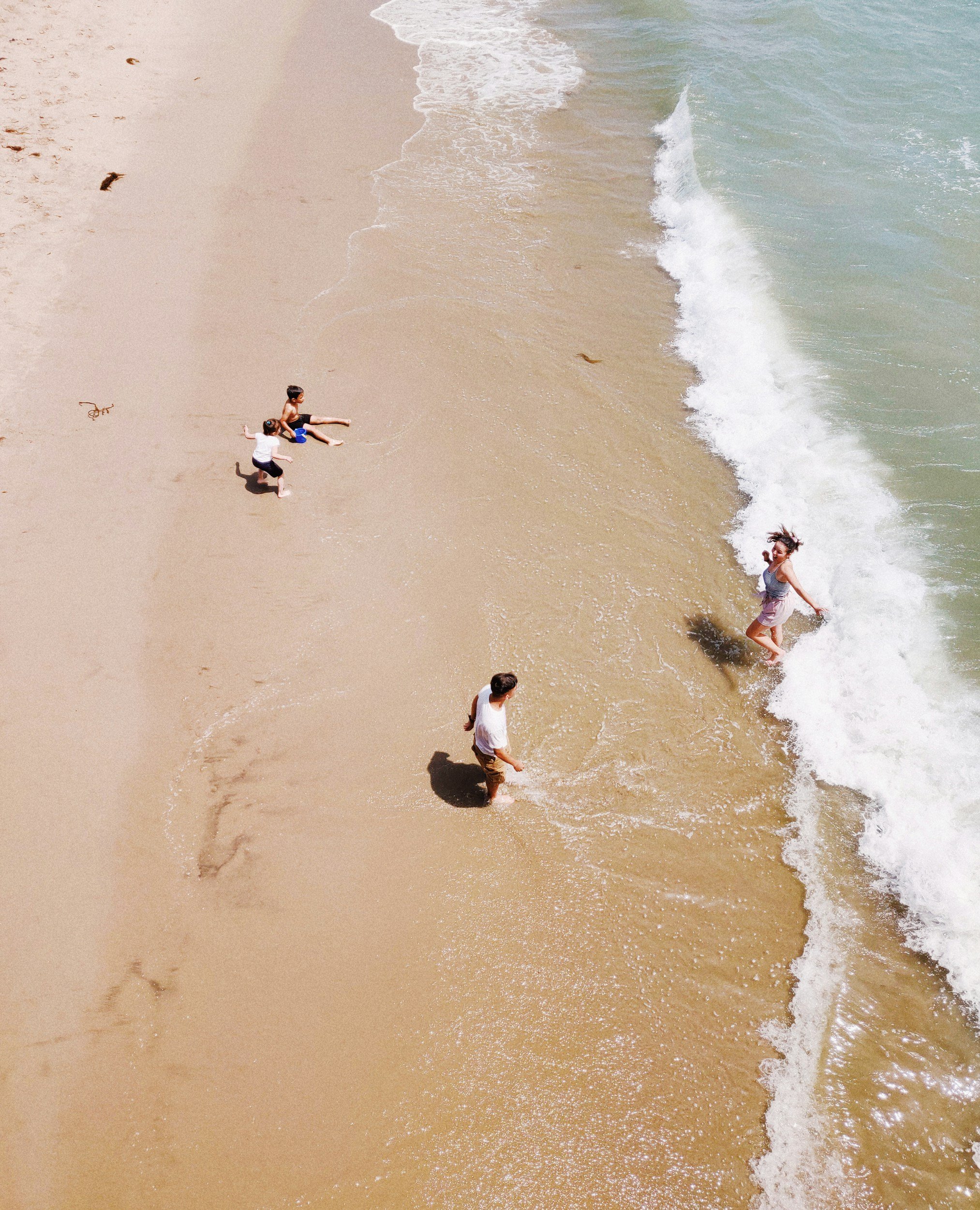 Bunbury Physio - People playing and sitting on the beach near the shoreline with ocean waves.