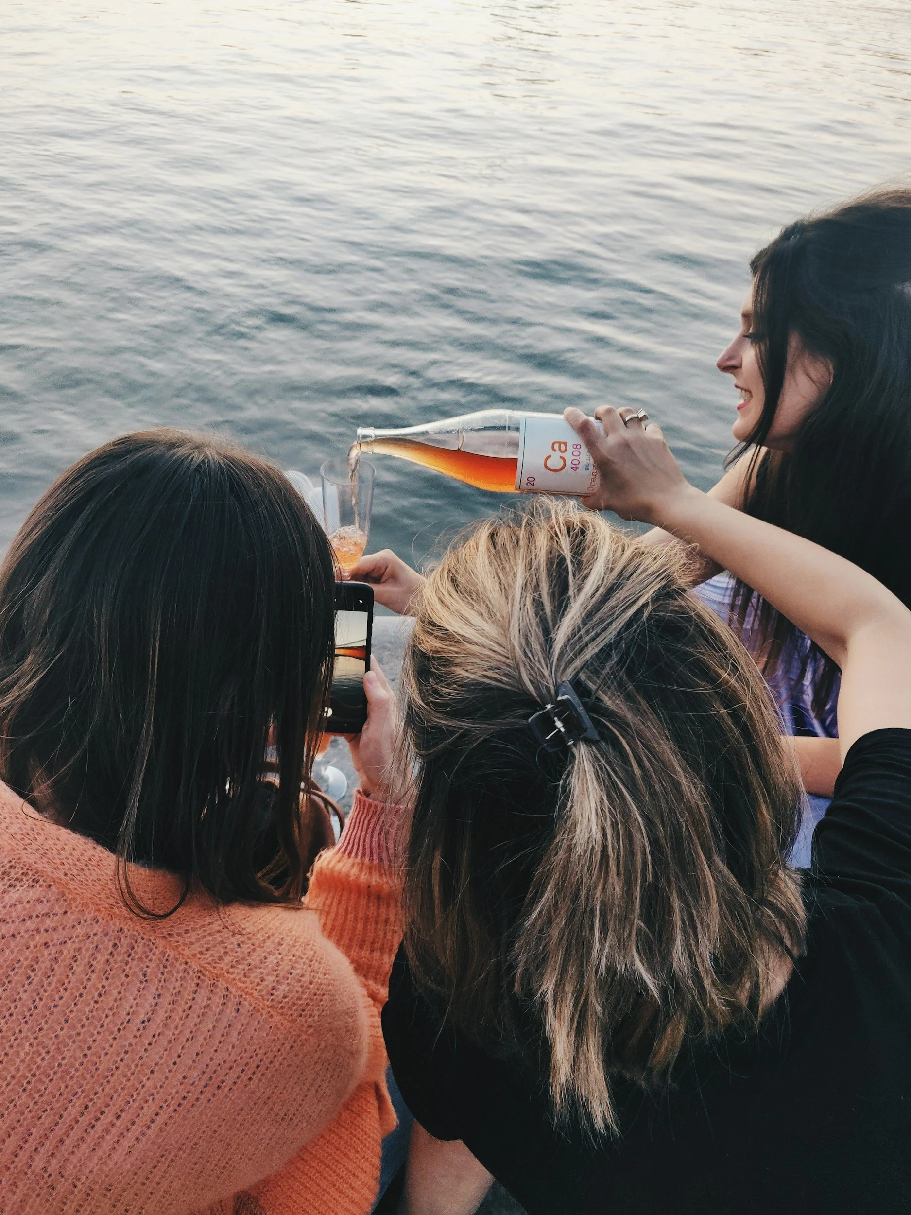 Bunbury Physio - Women on a boat, one pouring a drink into a glass while others watch, water in the background