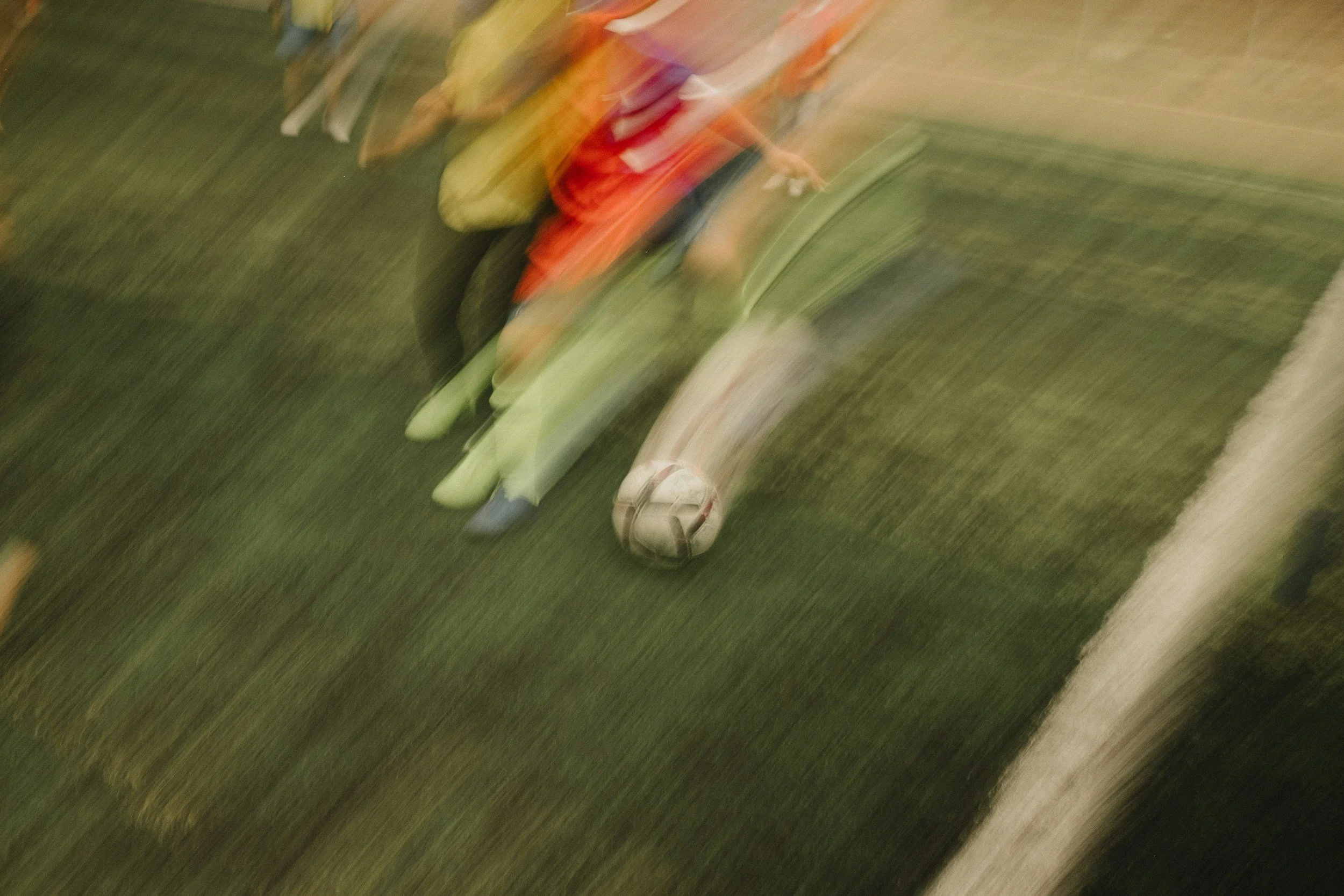 Bunbury Physio - A person playing soccer on a green turf field next to a white line, with a soccer ball near their feet. The image is blurry and appears to be in motion.