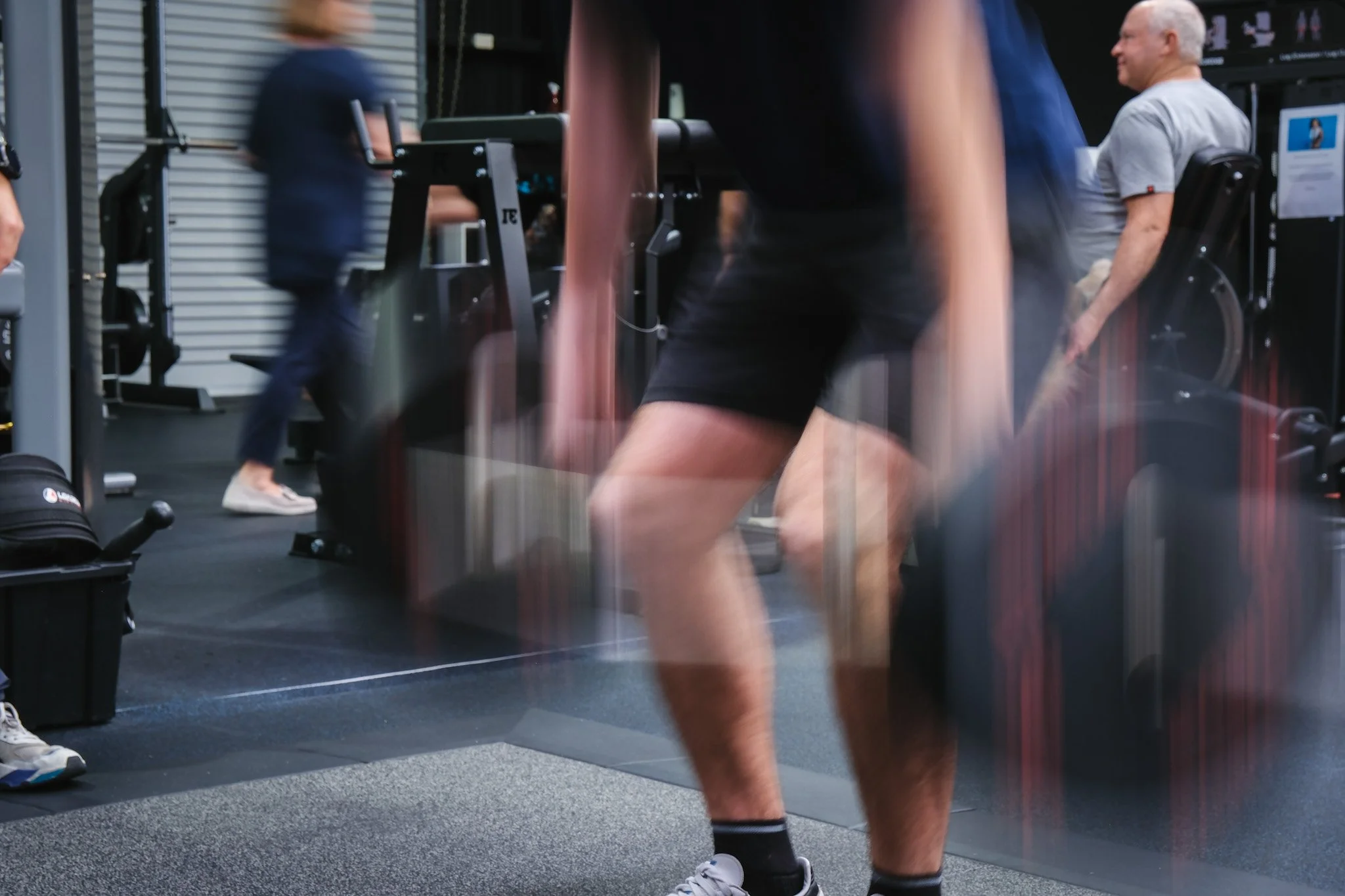 Bunbury Physio - Multiple people in gym engaged in exercises with fitness equipment, with focus on legs and some blurred movements.