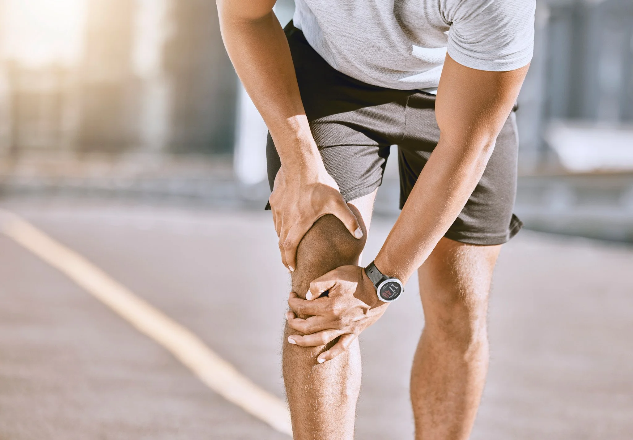 Bunbury Physio - An athlete in athletic clothing holding his knee, appearing to experience discomfort during a run or workout.