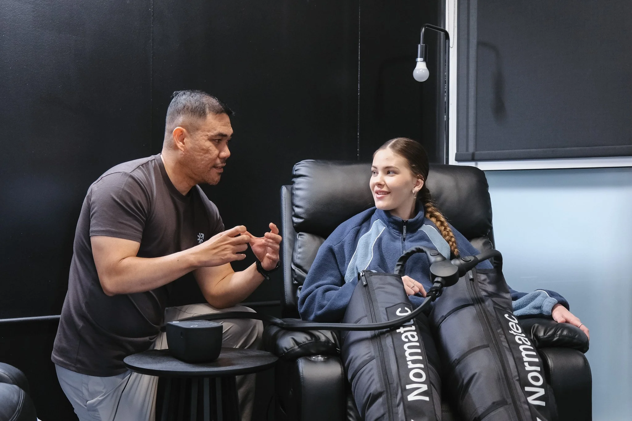 Bunbury Physio - A man and a young girl sitting in a room with black walls. The man is talking to the girl, who is seated in a wheelchair. There are golf clubs in a bag next to the girl.