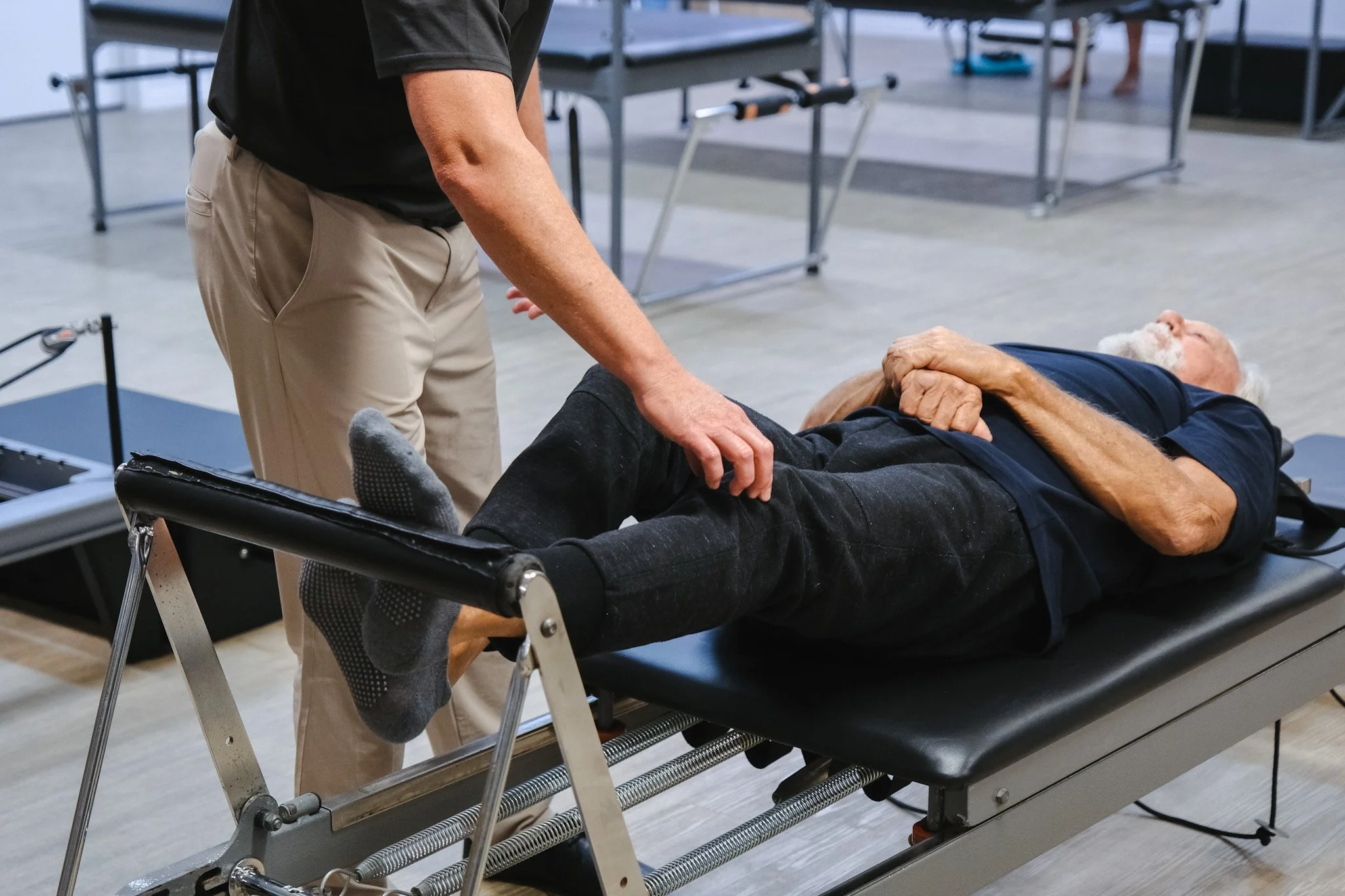 Bunbury Physio - A person lying on a medical examination table with their hand on their chest, being attended to by a healthcare professional in a clinical setting with medical equipment and other patients in the background.