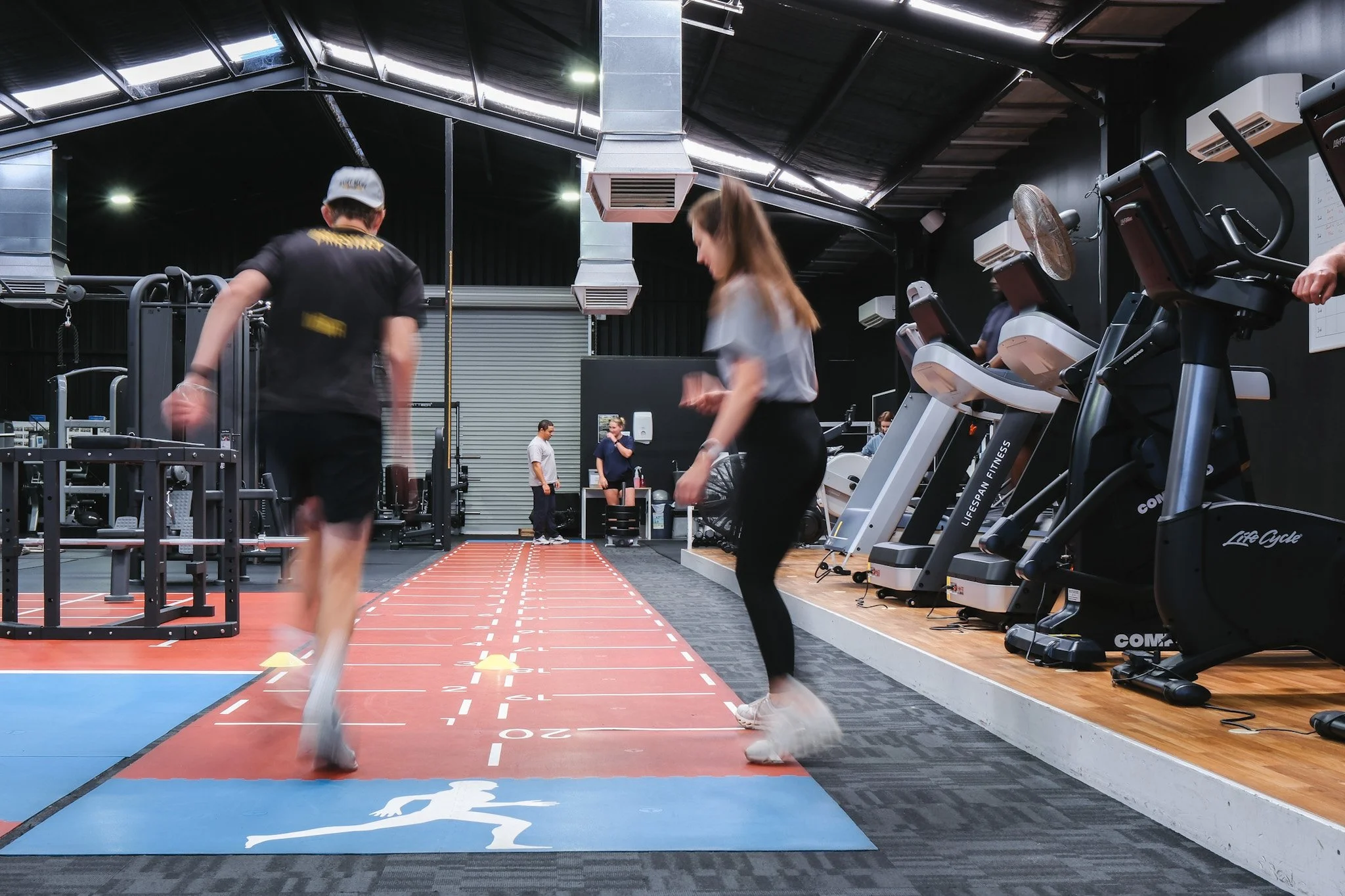 Bunbury Physio - People working out in a modern gym with fitness equipment including treadmills and a running track on the floor.