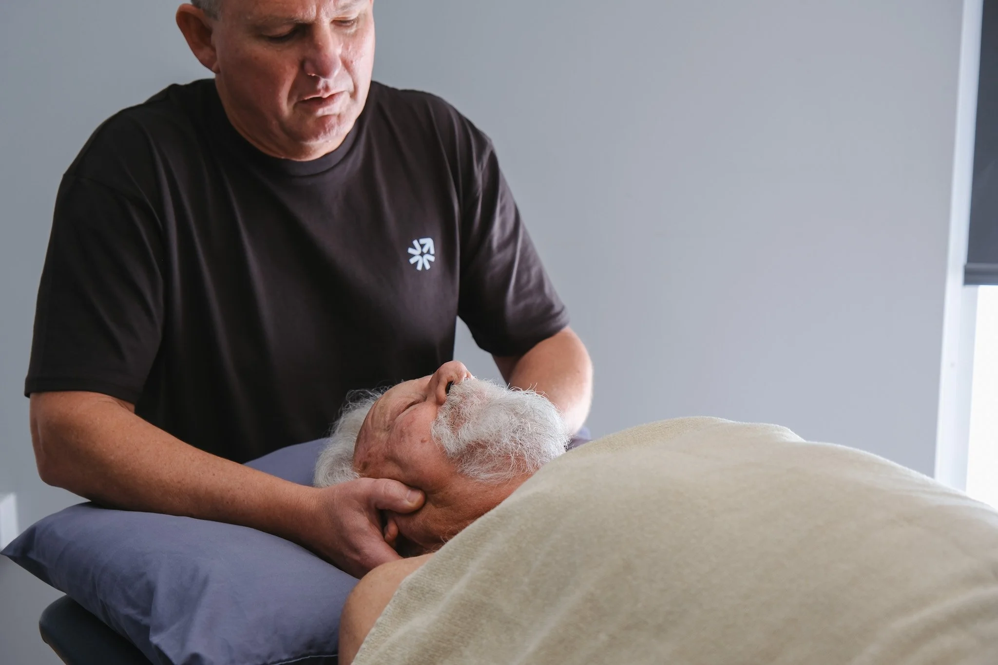 Bunbury Physio - A man providing a care service to an elderly person lying in a bed, in a clinical setting.