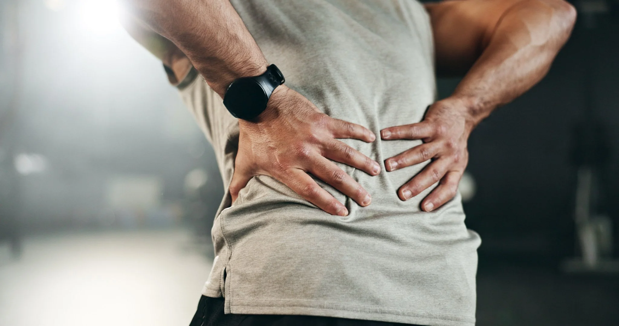 Bunbury Physio - Person standing with hands on lower back, wearing a smartwatch, in casual clothing, experiencing back pain.