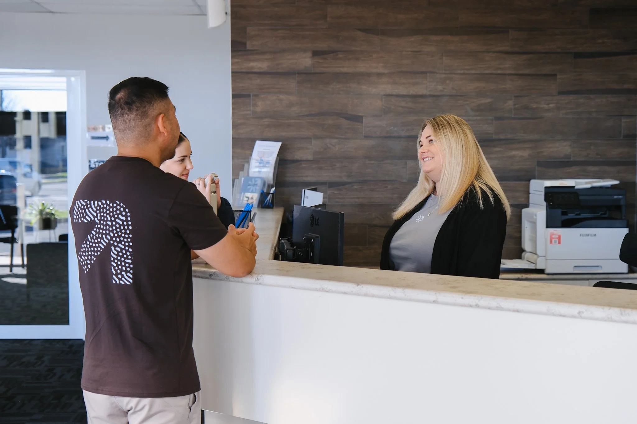 Bunbury Physio - A man and a woman at a reception desk in a modern office or hotel lobby, with the man smiling and the woman behind the desk smiling back.