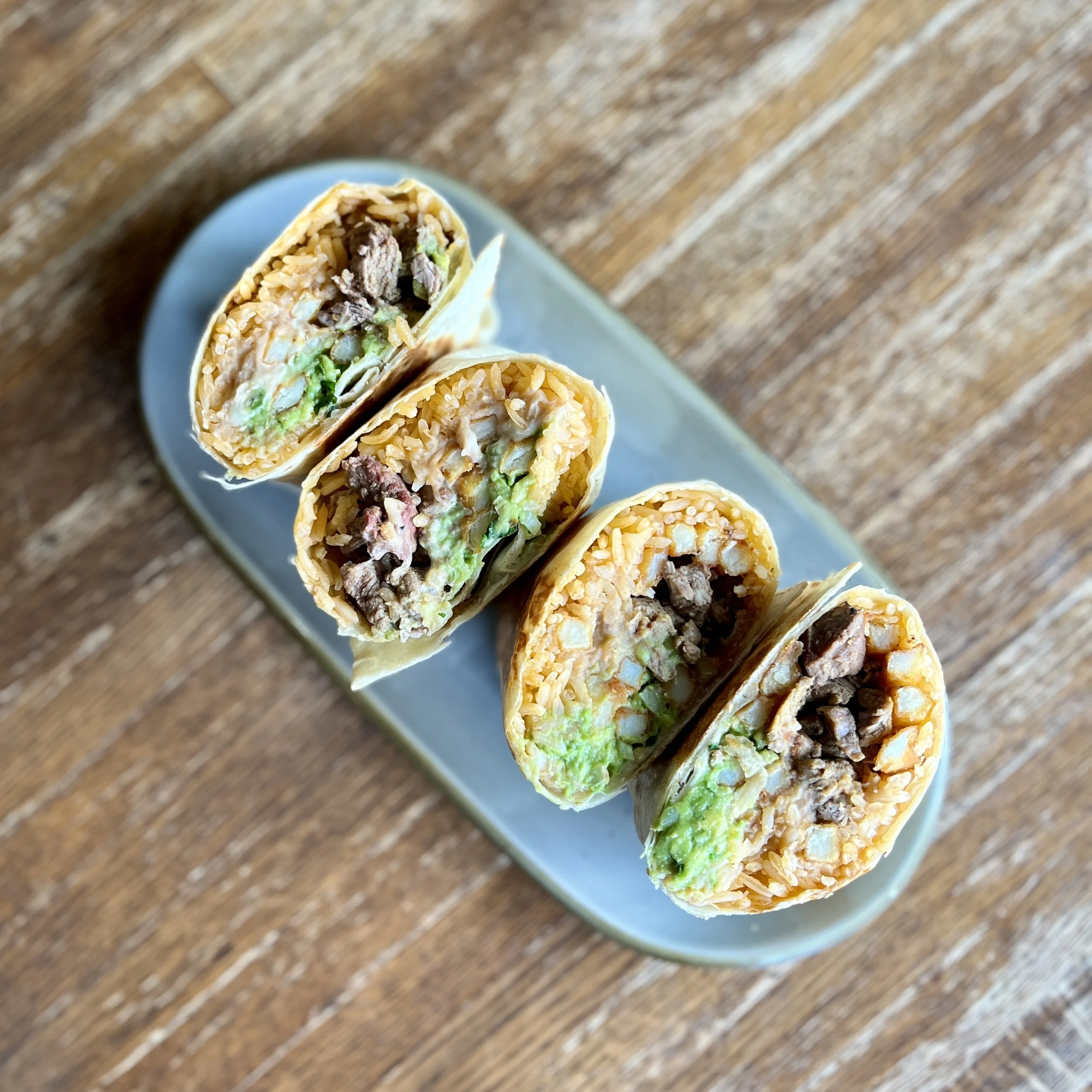 Close-up of sushi rolls filled with rice, beef, and vegetables on a blue plate, with a wooden table background.