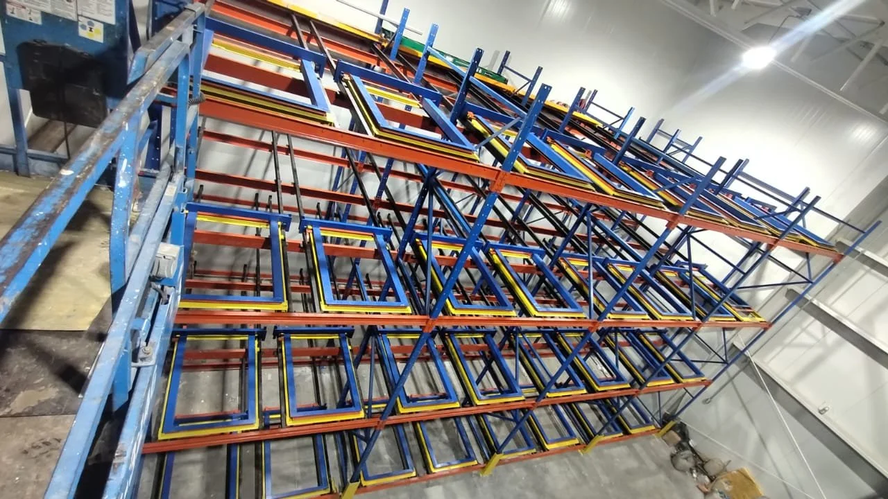 Estanterías de almacenamiento en un almacén industrial, con estructuras de metal pintadas en azul, naranja, y amarillo, sin cargas.