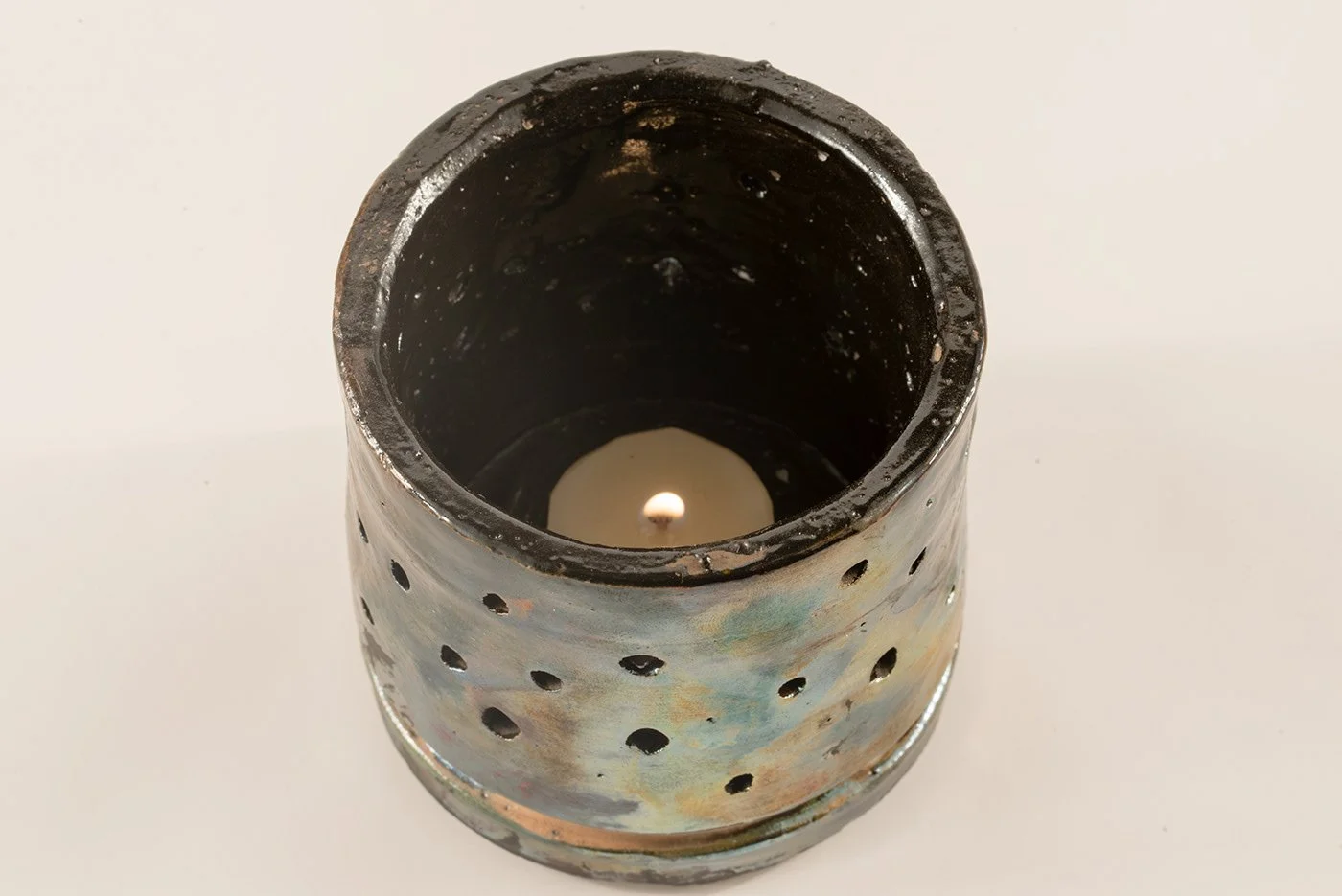 Ceramic tealight holder with a lit candle inside, viewed from above, on a white surface.