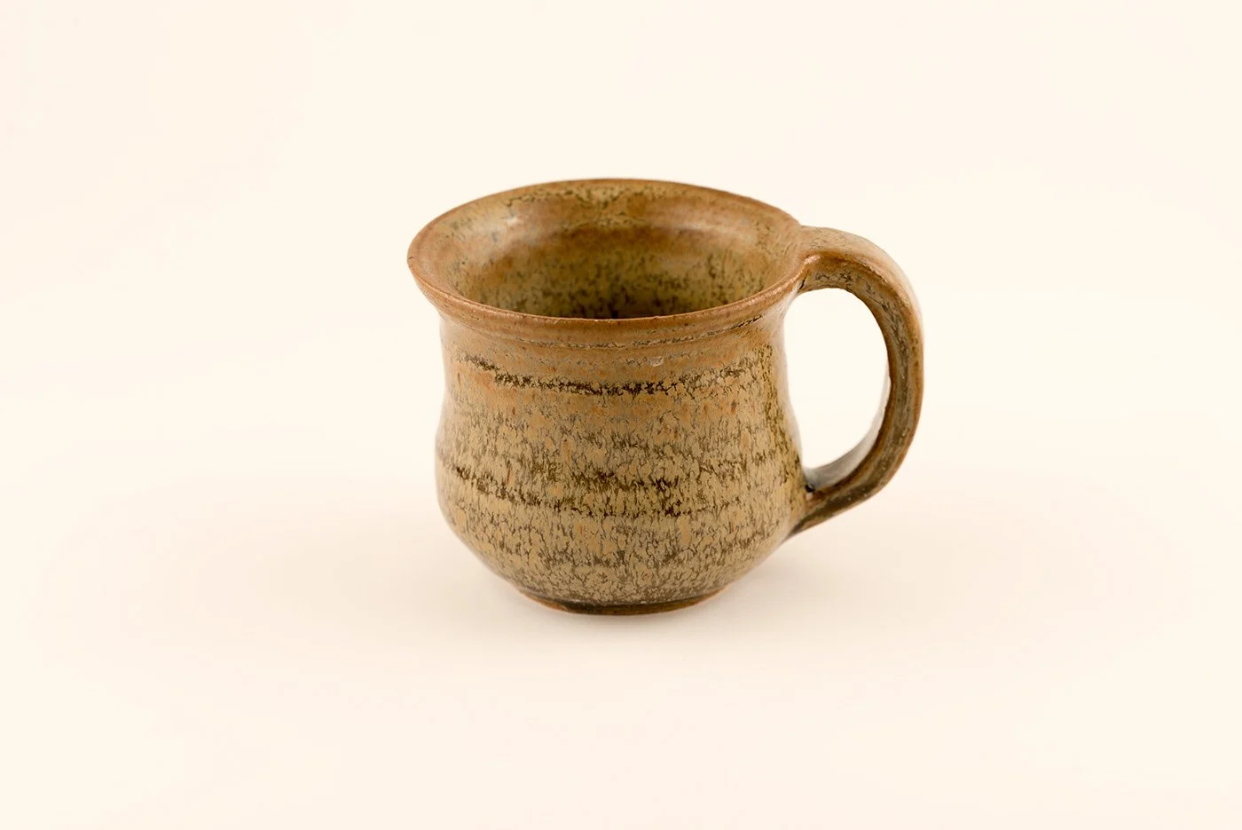 A rustic ceramic mug with a textured, crackled glaze, and a rounded handle, placed against a plain, light background.