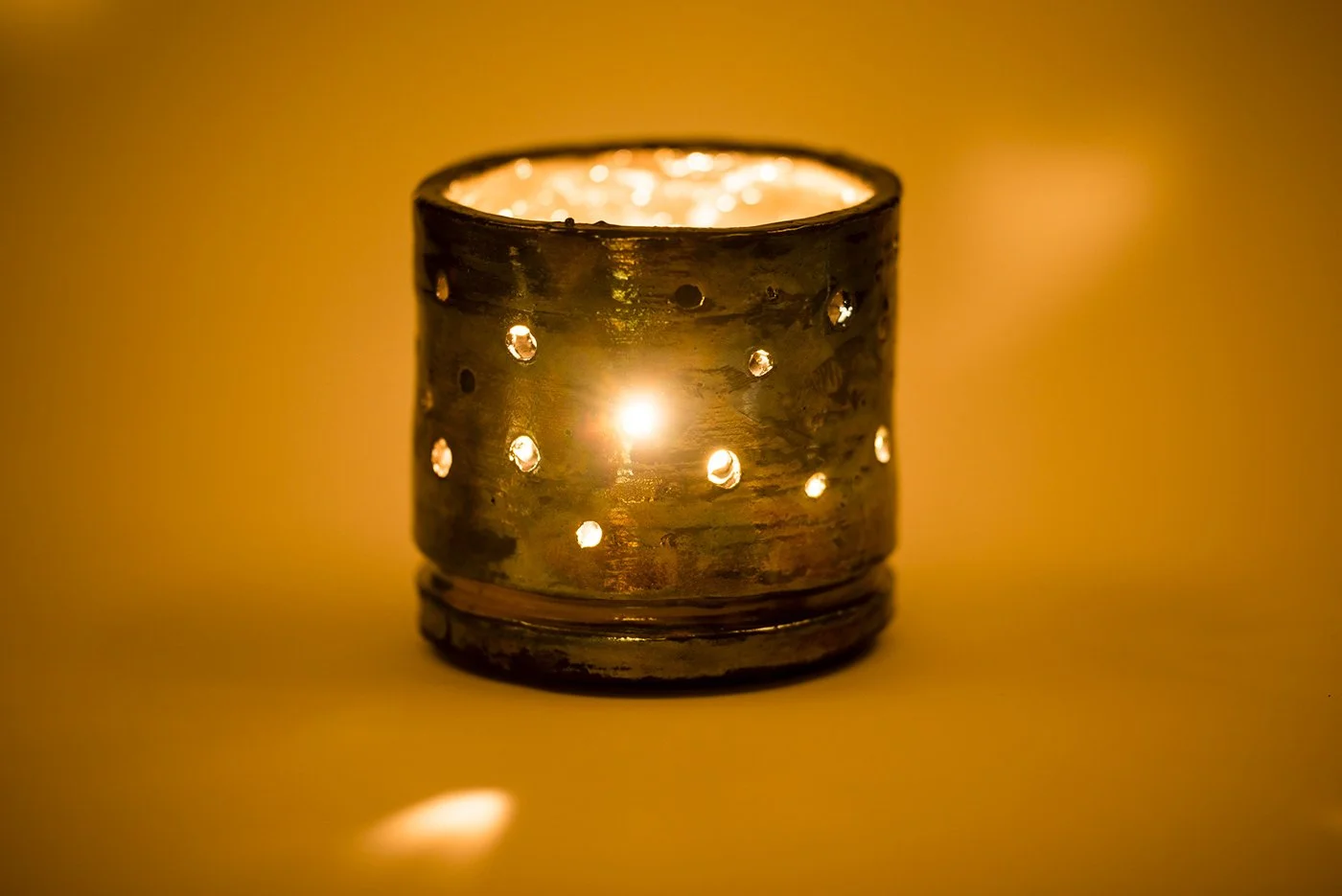 A metallic candle holder with small circular holes, containing a lit candle, creating a warm glow.