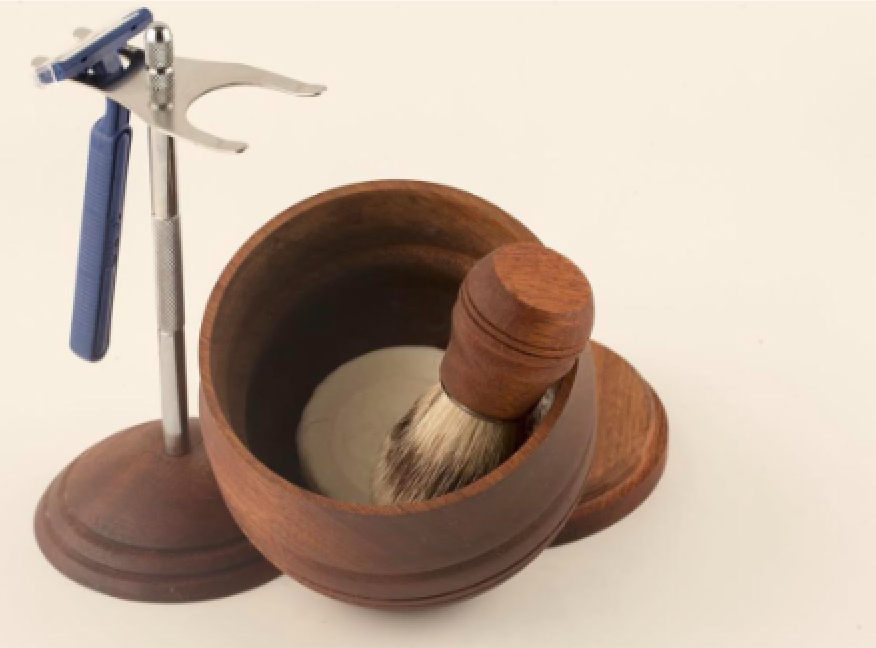 Vintage safety razor, shaving brush inside wooden bowl, and wooden stand with razor on a white surface.