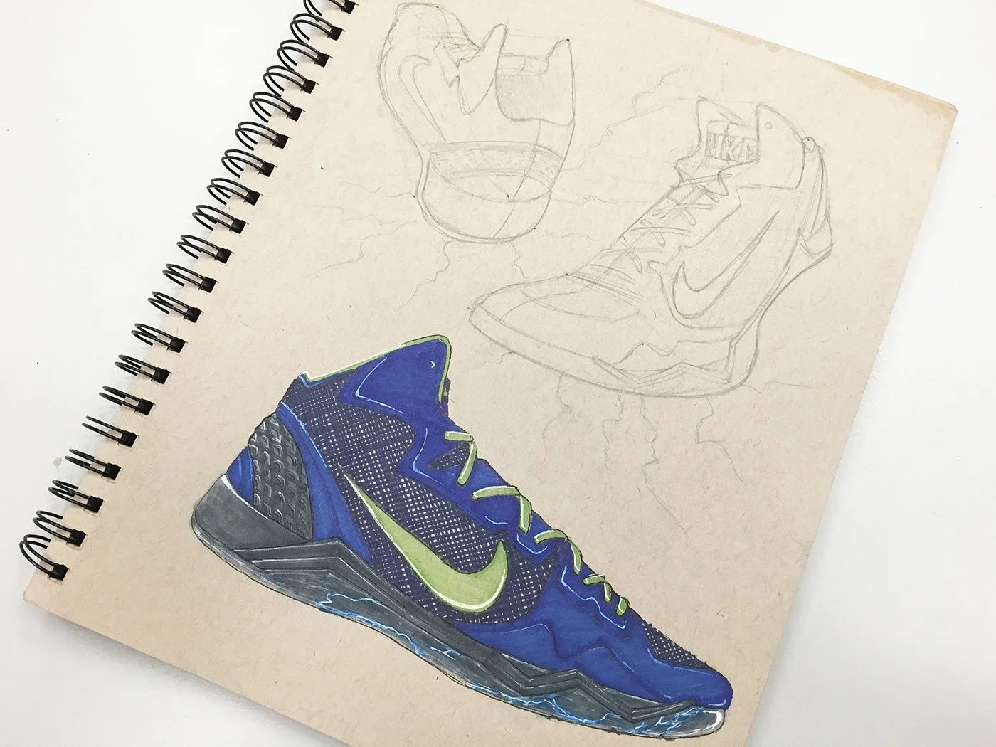 Sketches of sneakers and a cup, with a colored drawing of a blue and green sneaker on a spiral-bound sketchpad.
