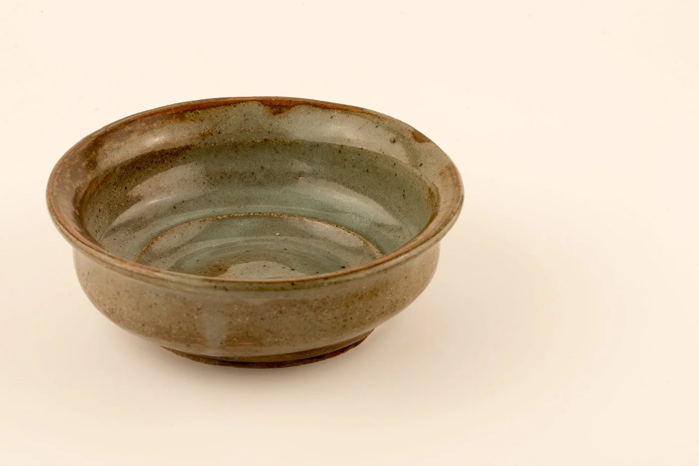 A ceramic bowl with a glaze finish, featuring natural earthy tones and a subtle spiral pattern, set against a plain white background.