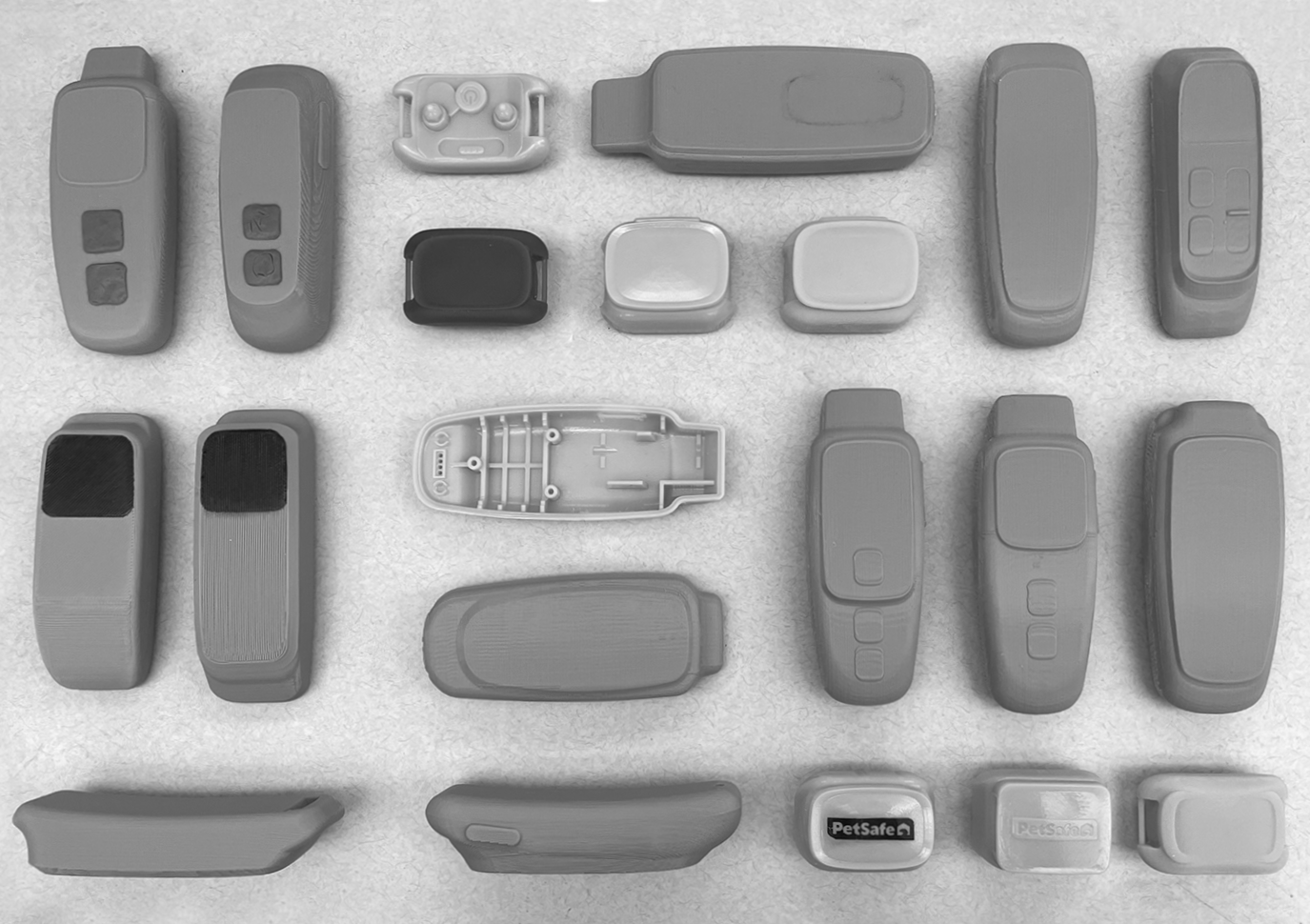Collection of various remote controls, key fobs, and electronic device pieces arranged on a light surface in black, gray, and white colors.