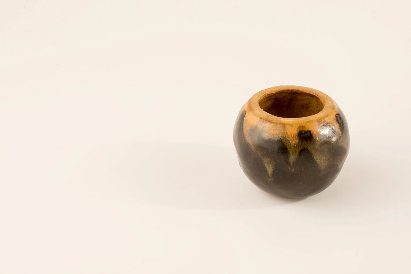 A small round ceramic vessel with a brown and black glazed exterior, viewed from above on a white background.