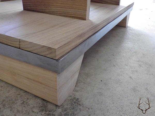 Close-up of a wooden bench with a metal accents at the base, positioned on a concrete floor.