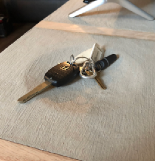Car key with remote, attached to keychain, resting on a beige placemat on a wooden table.