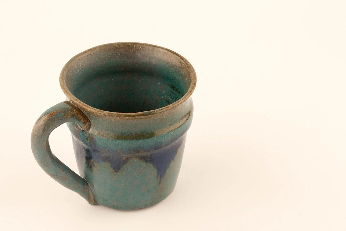 A ceramic mug with a greenish glaze, with the interior and exterior visible, placed on a plain white background.