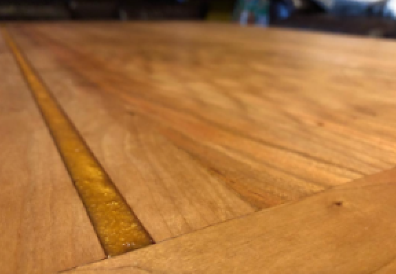 Close-up of a wooden table with a narrow crack showing aged, yellowed glue or filler.