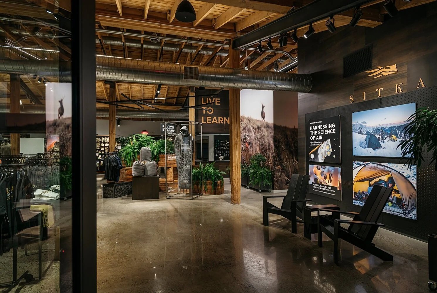 Interior of a retail store with wooden beams, industrial ducts, and natural decor. Display includes outdoor adventure gear and posters about air science and camping.
