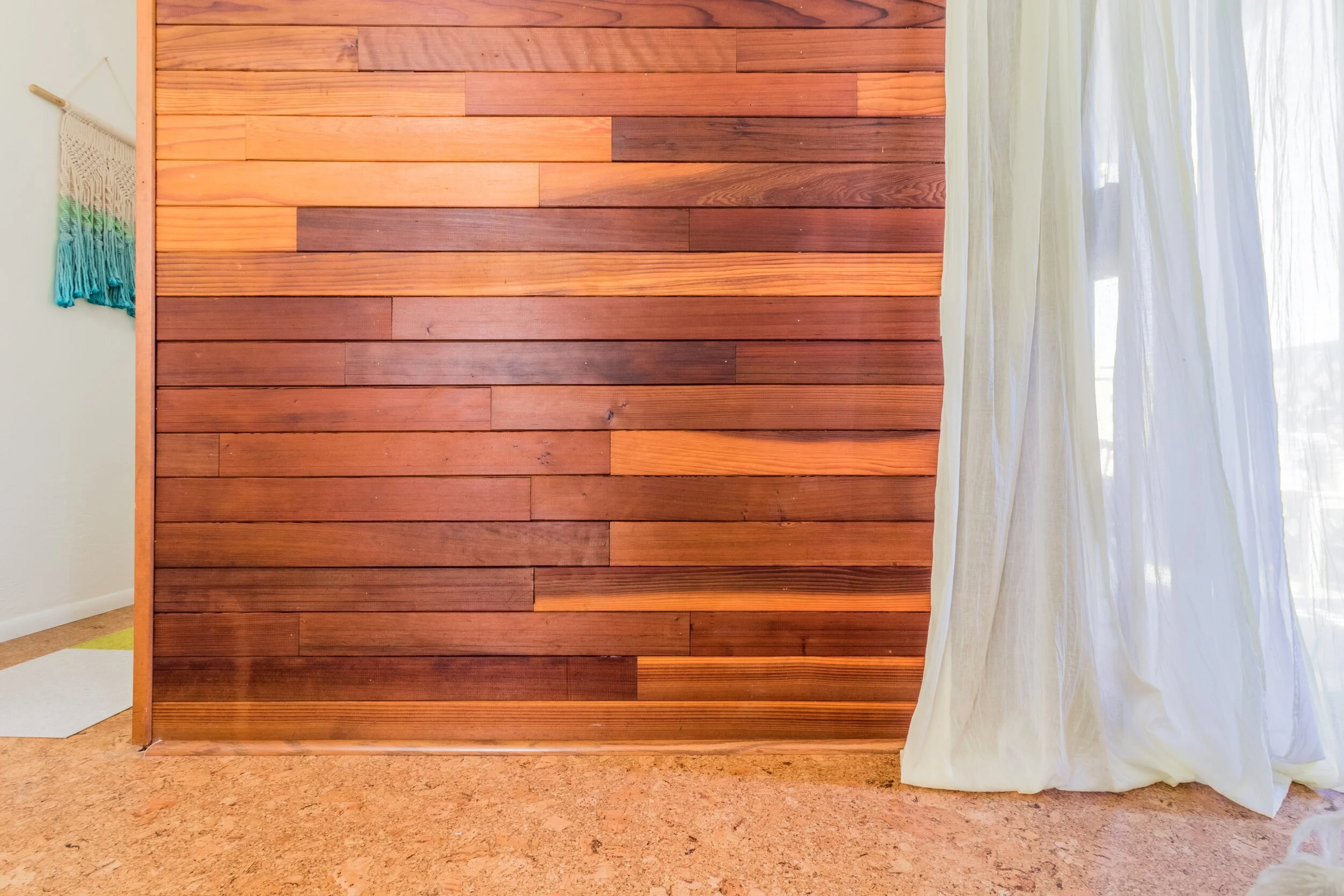 Interior room with wood-paneled wall, cream-colored curtain, and beige carpeted floor.